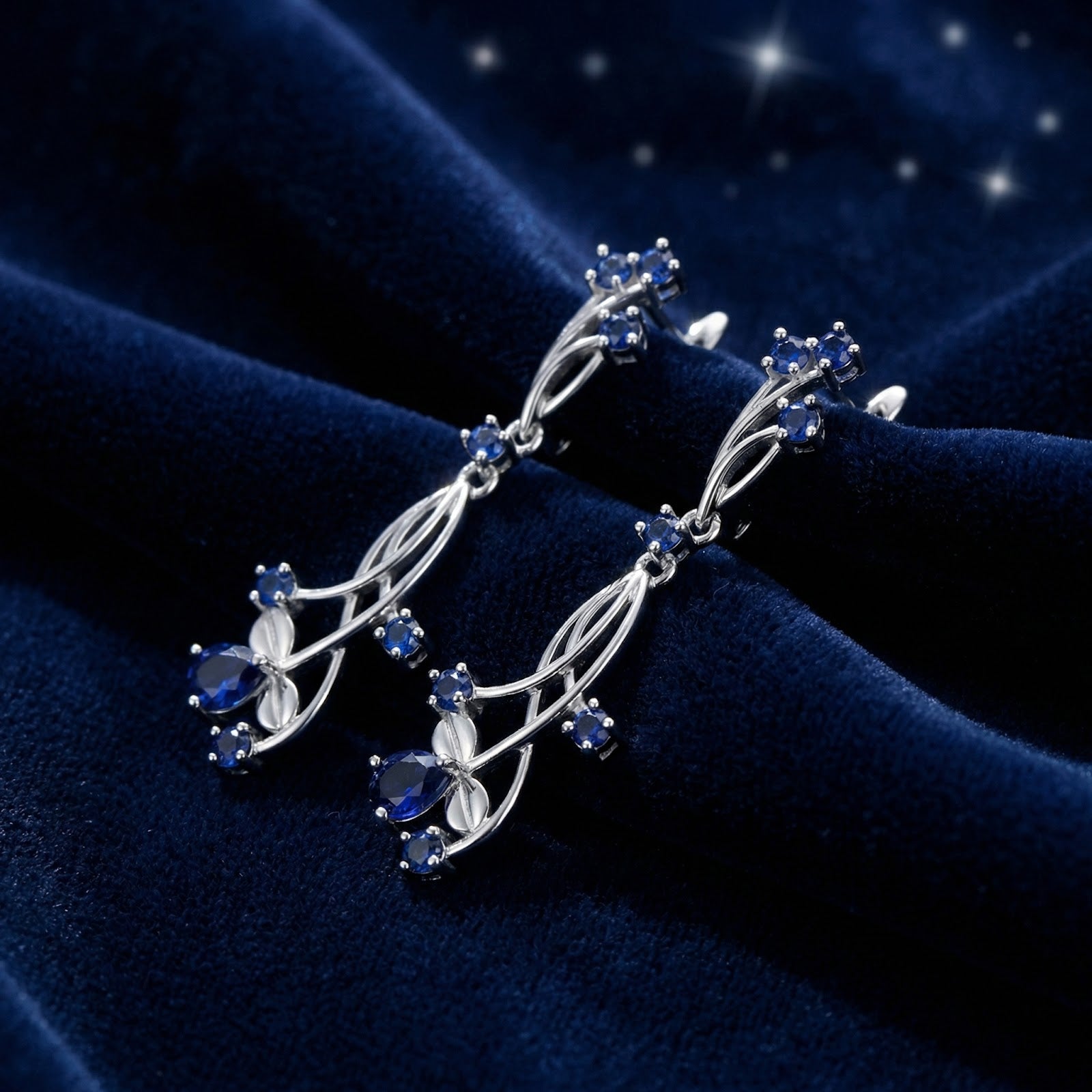 Side view of sterling silver vine drop earrings featuring deep blue simulated sapphires on a velvet background.