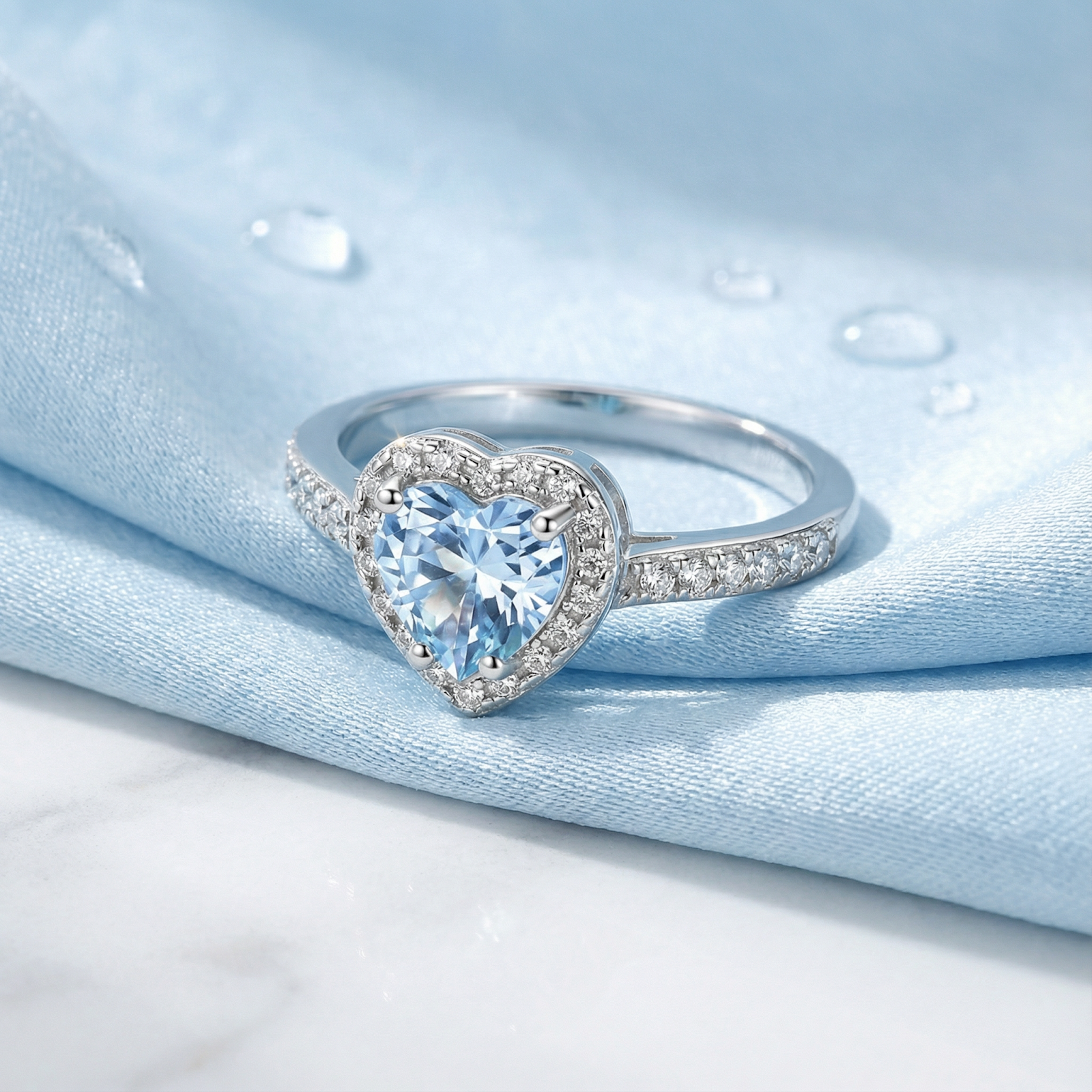 Macro view of a heart-cut simulated aquamarine sterling silver ring with a halo setting on blue silk.