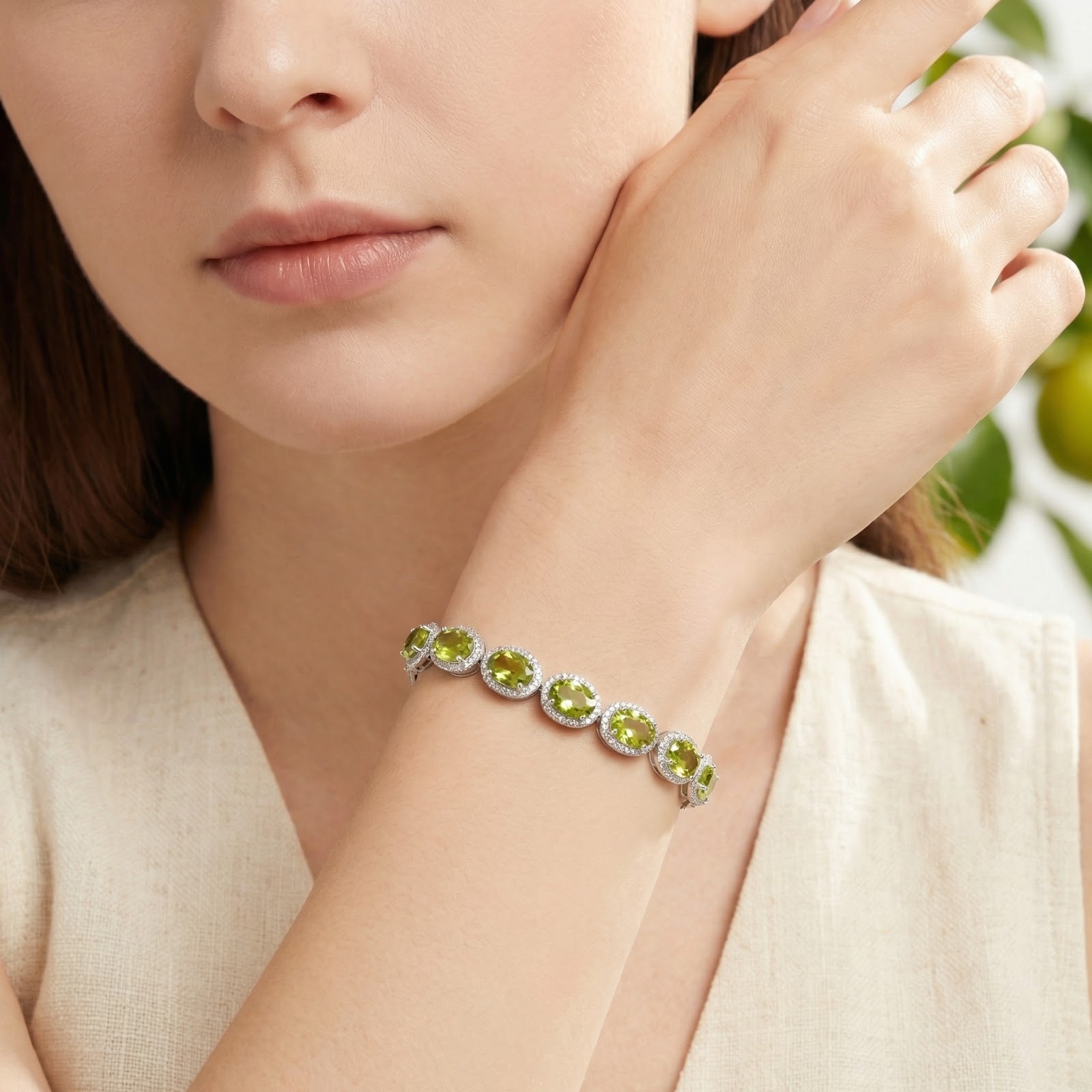 Sterling silver tennis bracelet with oval yellow-green simulated peridot stones worn on a woman's wrist.