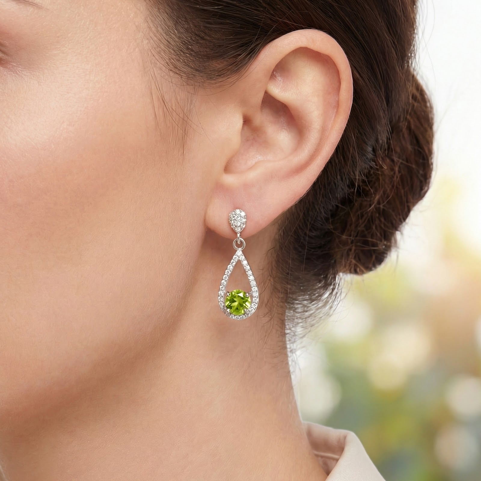 Detailed view of a sterling silver teardrop earring with a round simulated peridot stone worn on an ear.