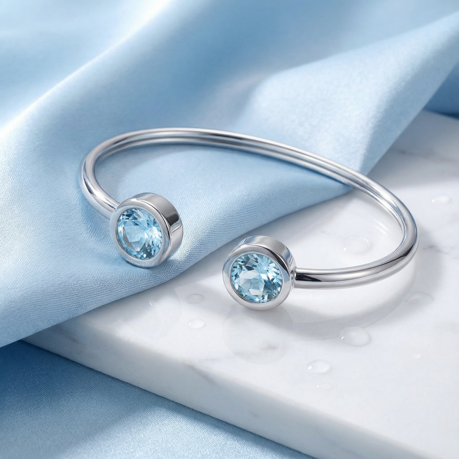 Close-up of round-cut simulated aquamarine stones on a silver stainless steel Cyrene bangle.