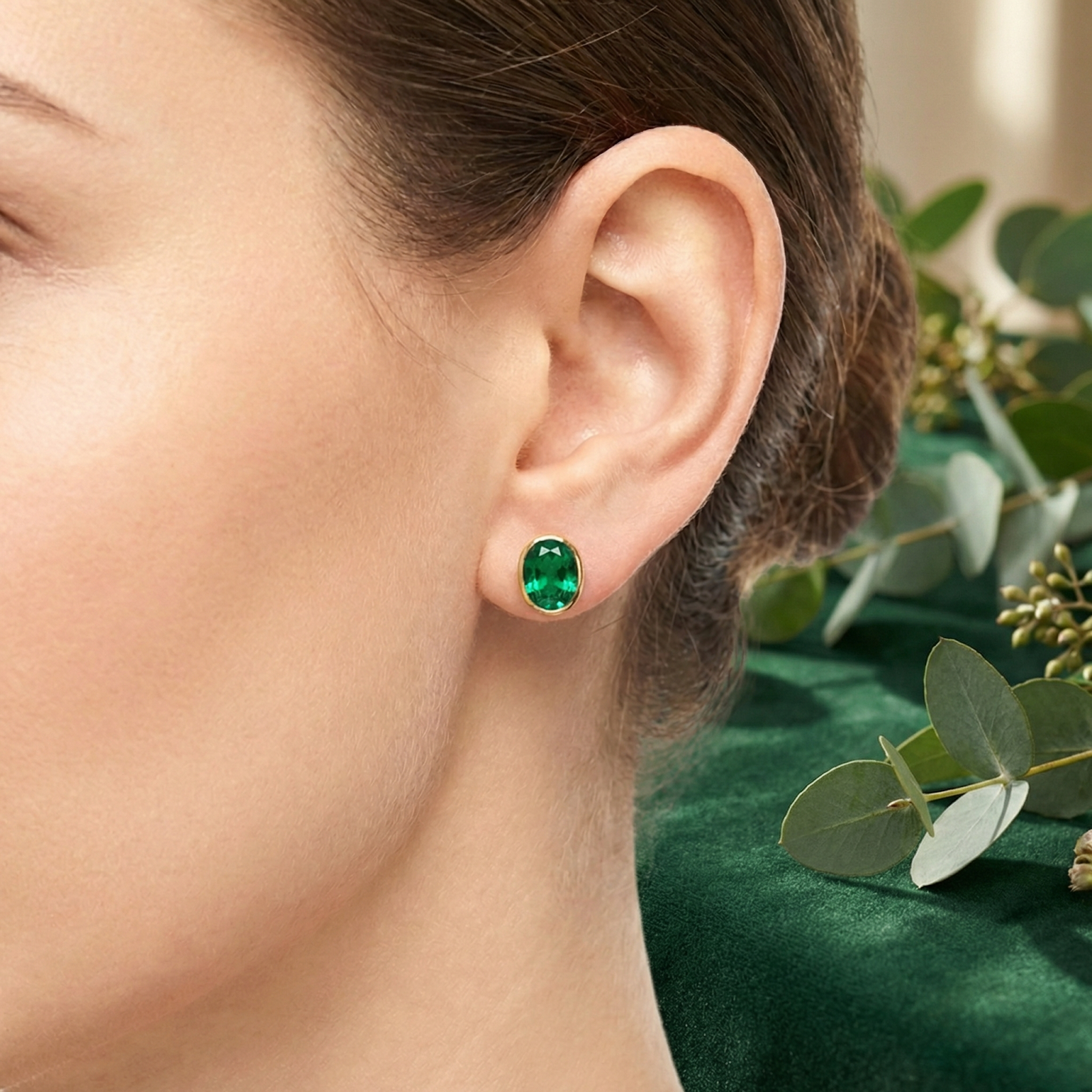 Close-up of a woman wearing The Veris Oval 18K gold plated simulated emerald earring on her ear.