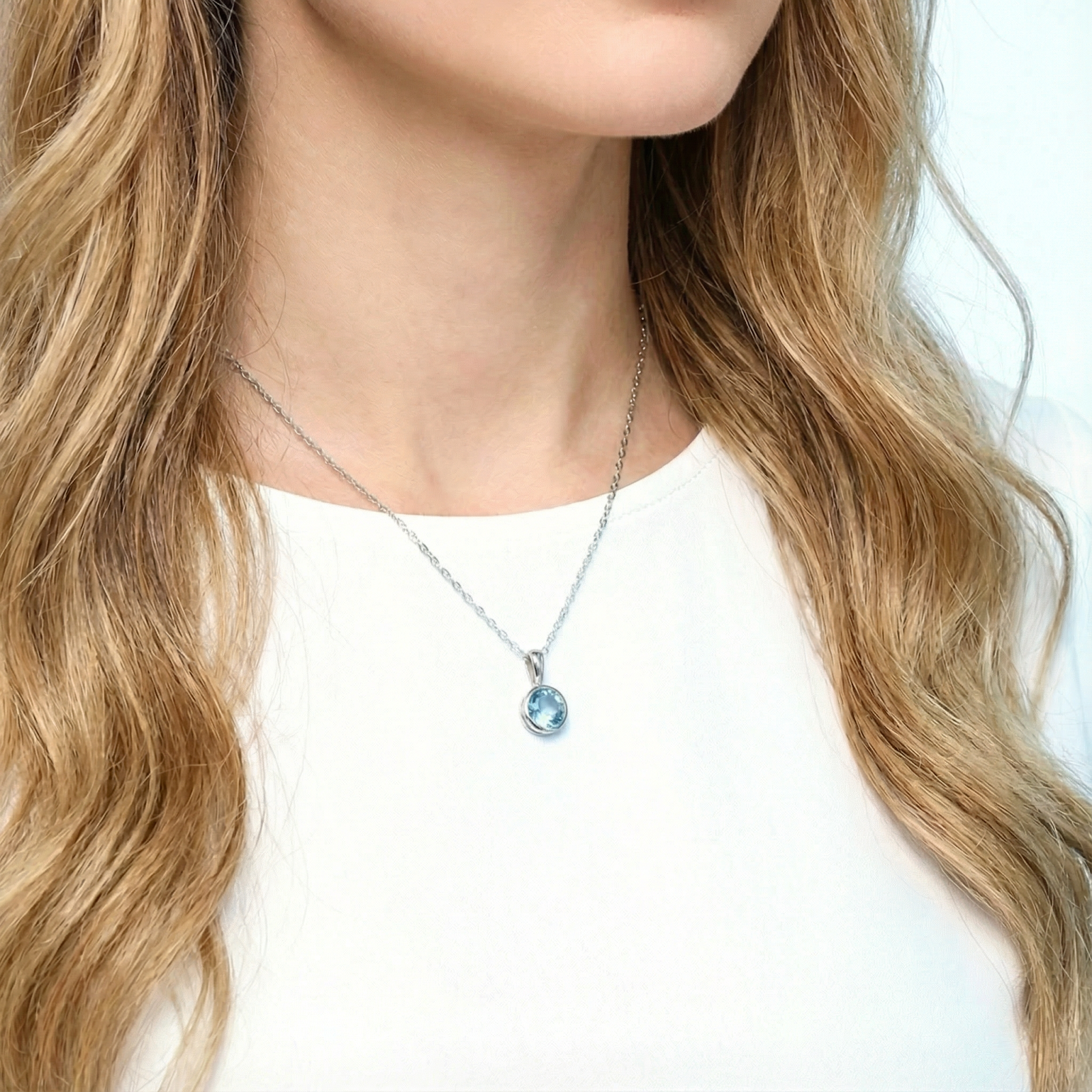Woman wearing the Marella sterling silver necklace with a round light blue simulated aquamarine pendant.