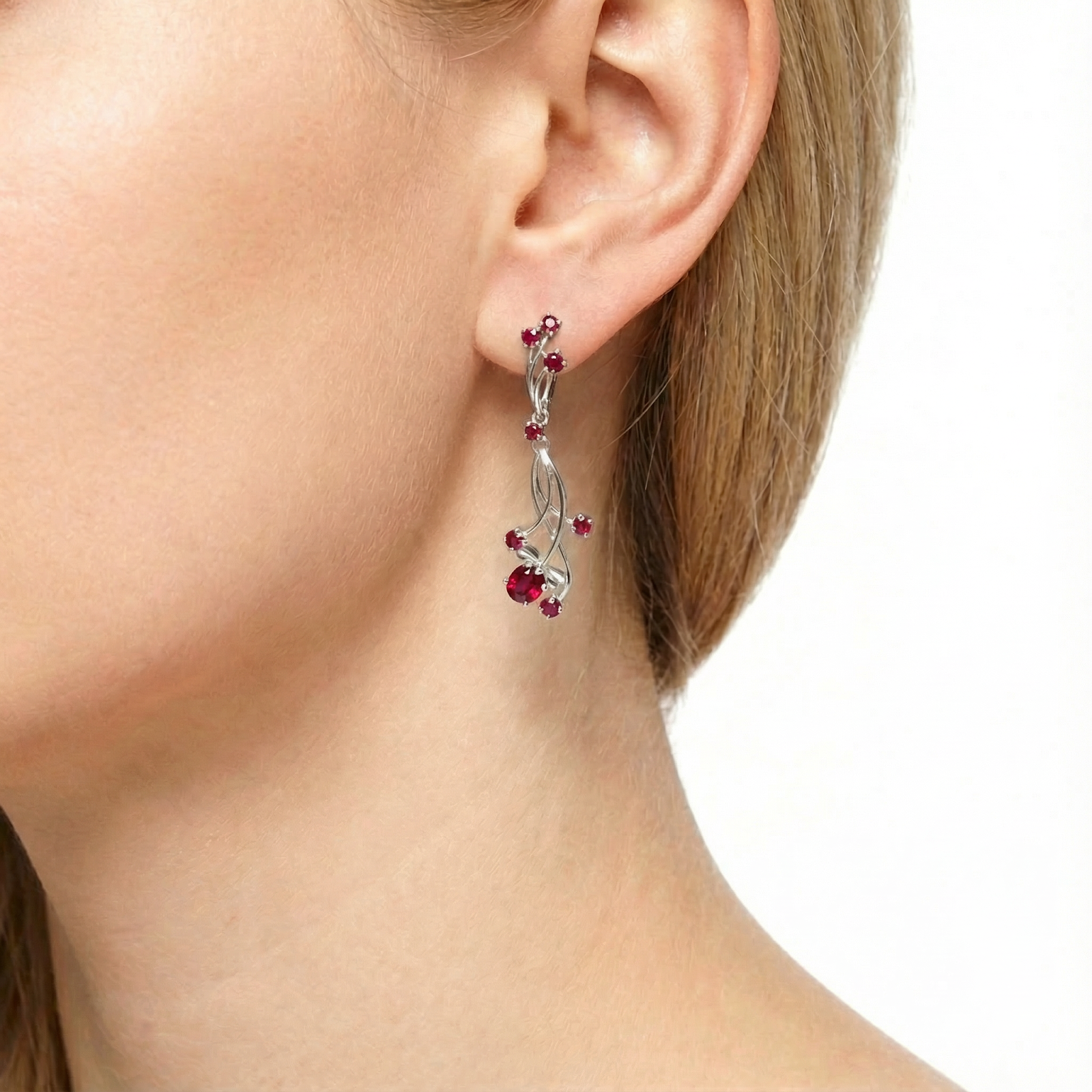 Close-up of a sterling silver drop earring with round and pear-cut simulated rubies worn on a model's ear.