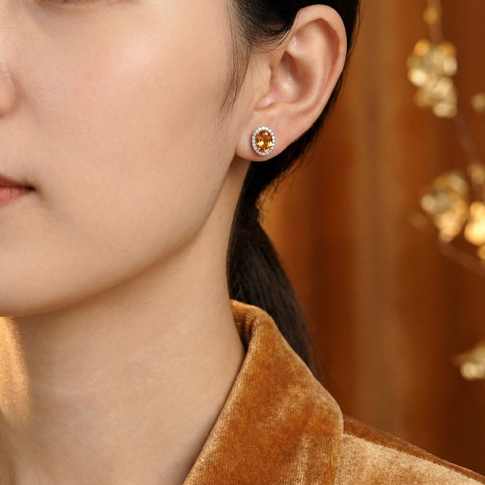 Woman wearing an oval honey-colored simulated topaz halo stud earring in S925 sterling silver on her ear.