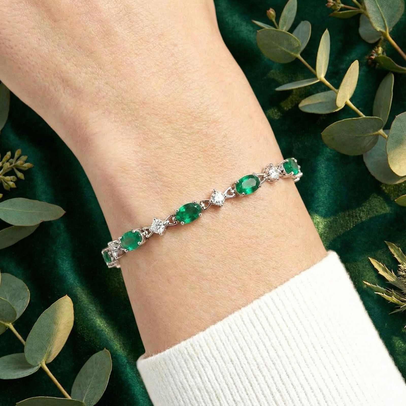 Close-up of a silver bracelet with oval simulated emeralds worn on a woman's wrist.