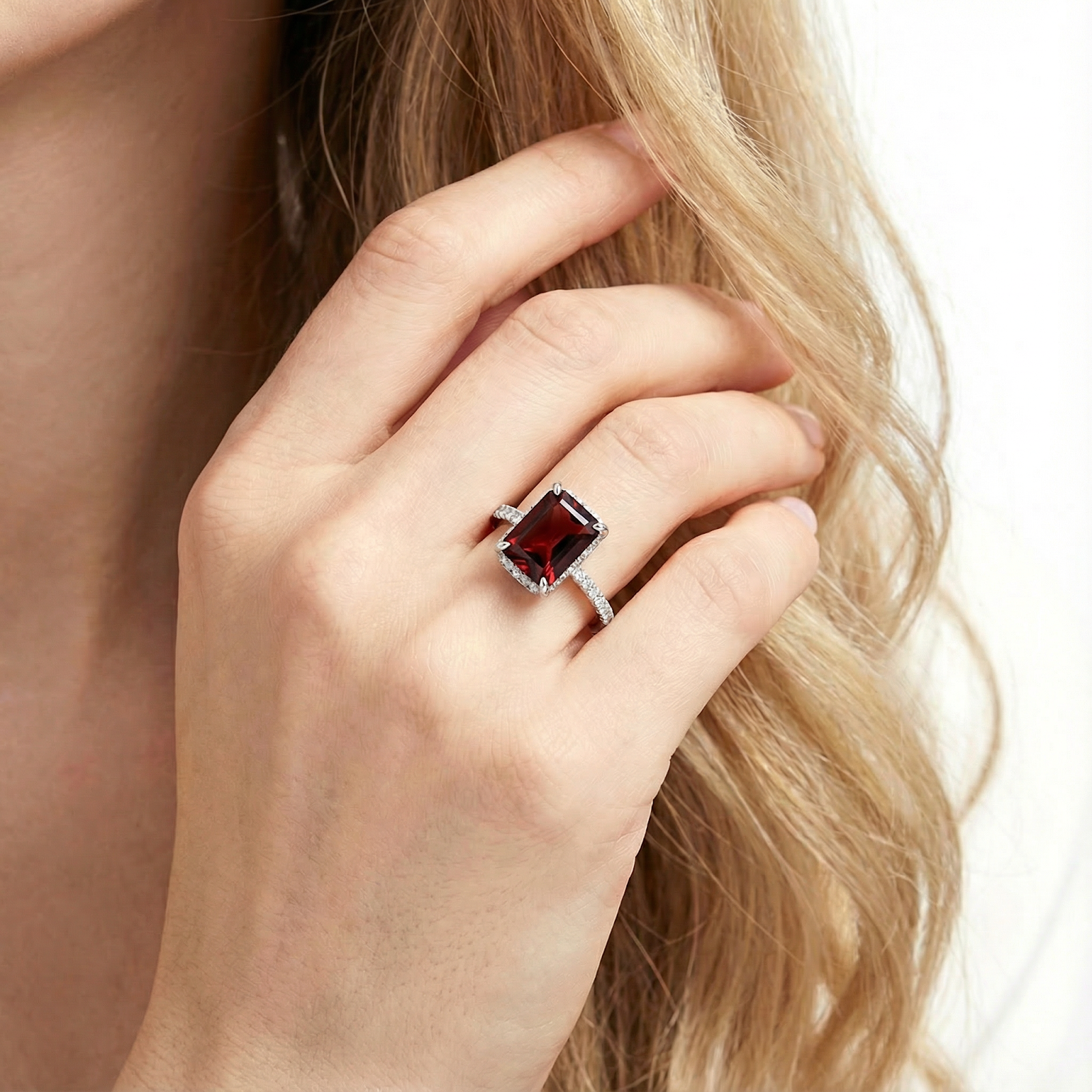 Radiant cut red garnet sterling silver ring worn on a woman's hand against her blonde hair.