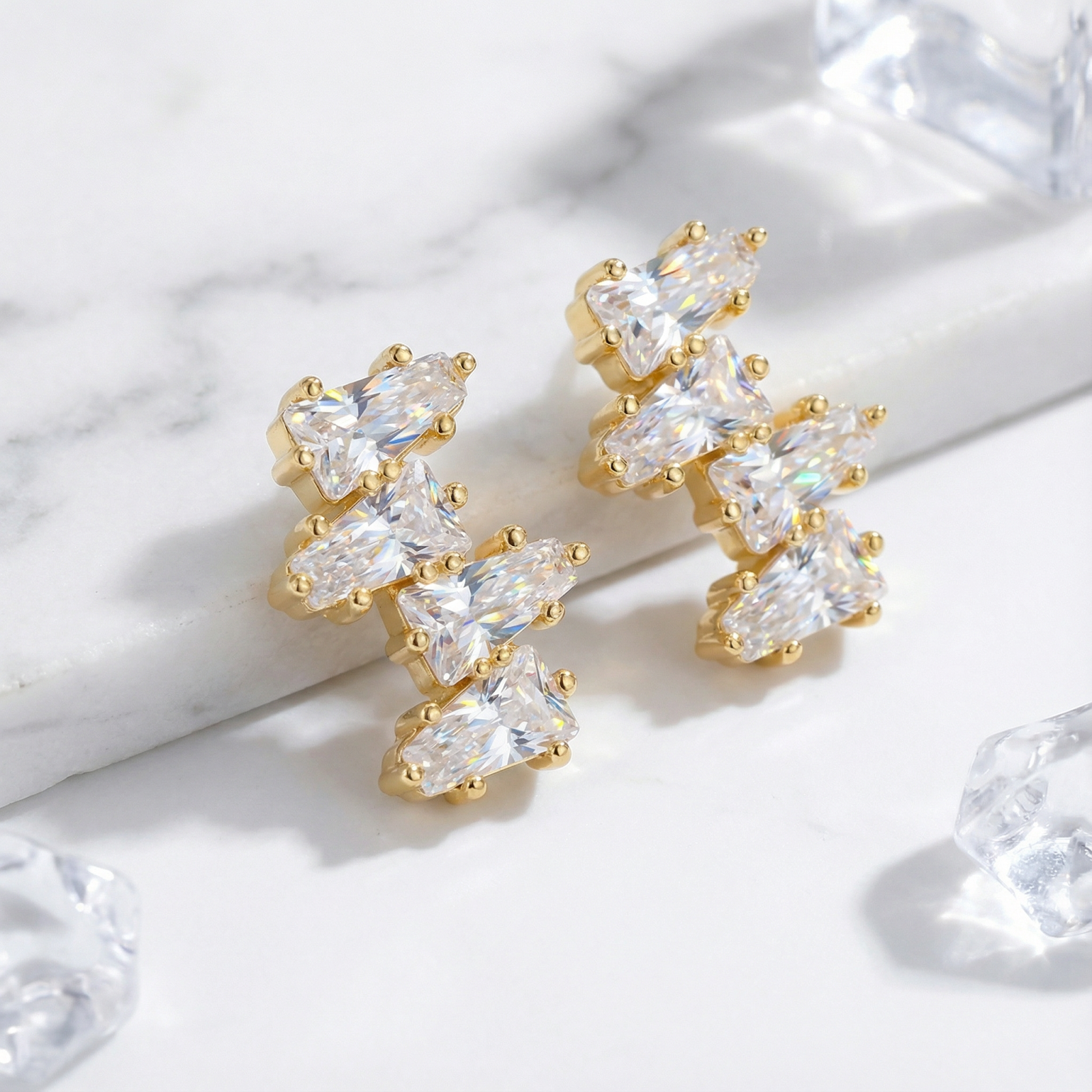 18K gold vermeil cluster earrings with tapered baguette zirconia stones on a marble surface with ice props.
