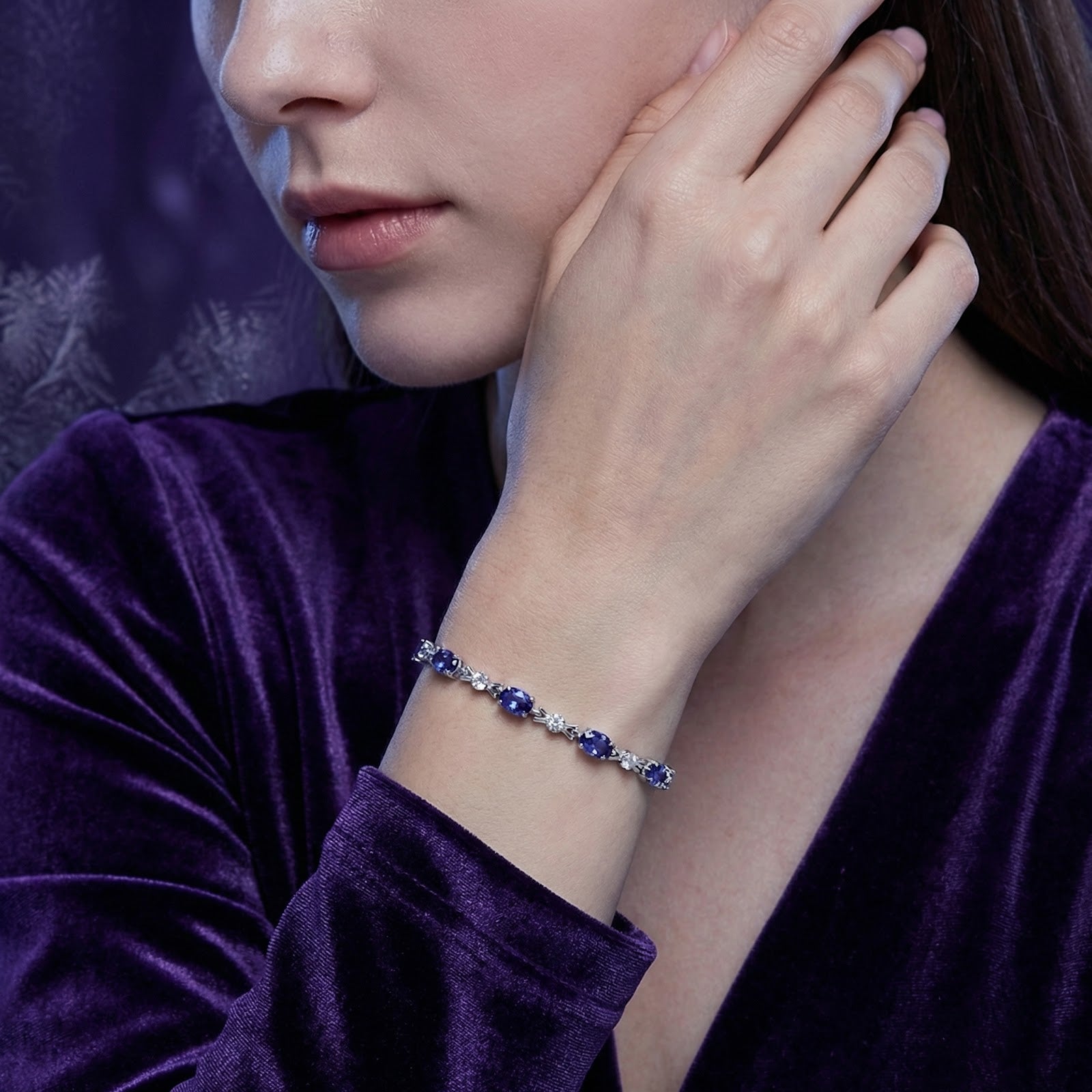 Woman wearing the Elaraea oval simulated tanzanite sterling silver bracelet with a purple velvet dress.