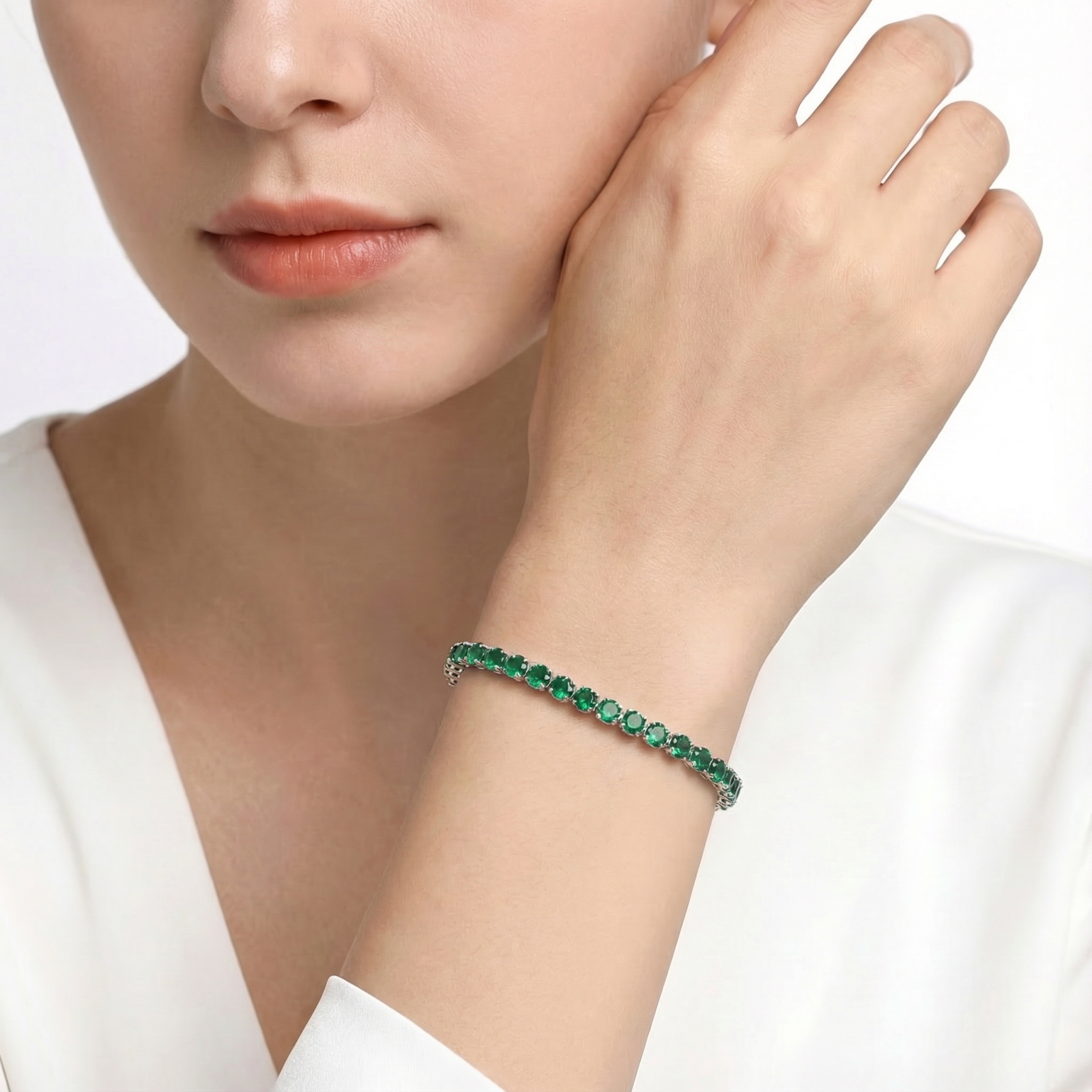 Stainless steel tennis bracelet with May birthstone simulated emeralds worn on a woman's wrist.