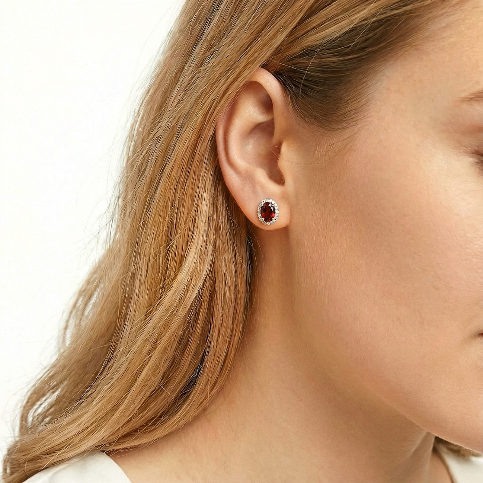 Side view of a woman wearing the Zenobia oval simulated garnet halo stud earring in sterling silver.