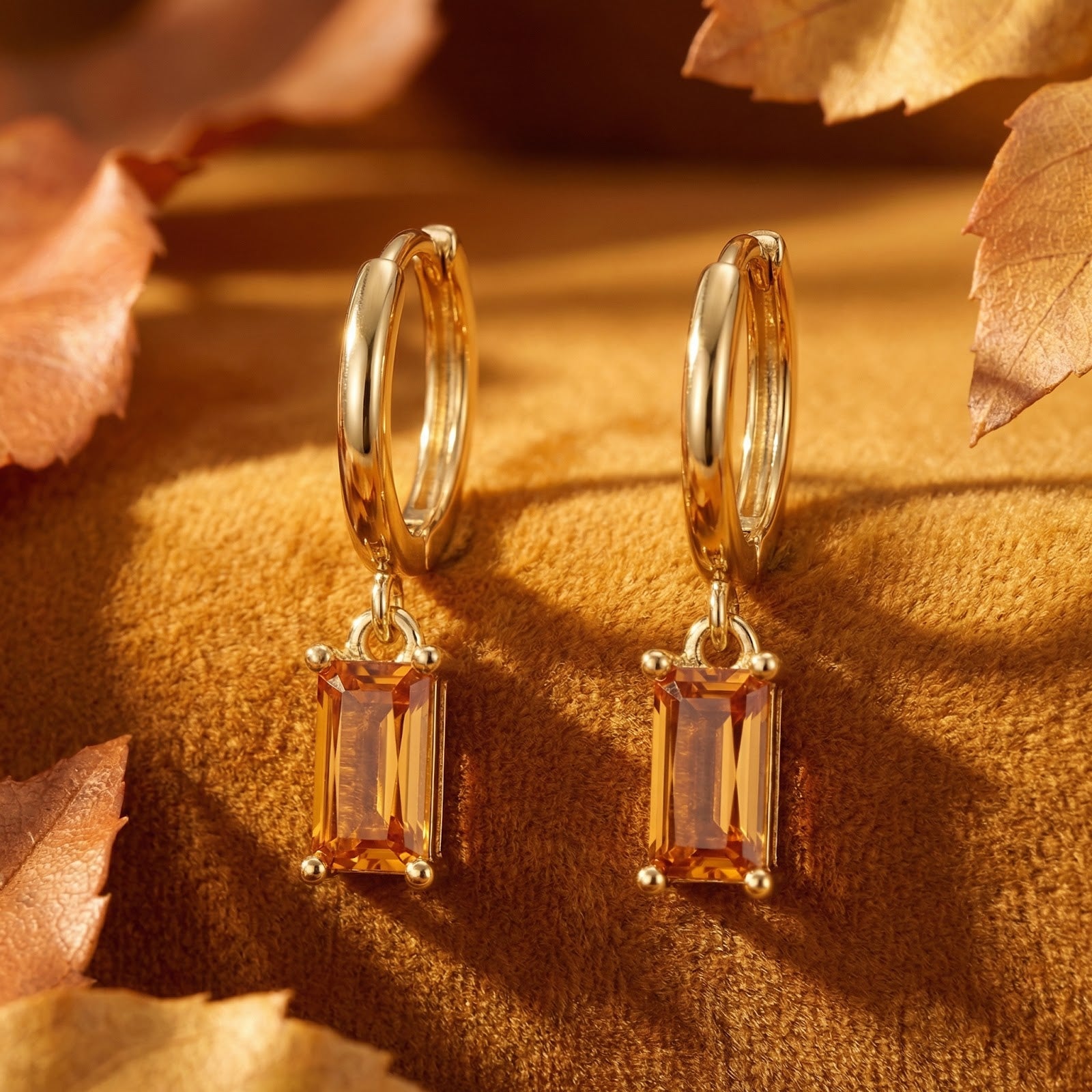 Detail view of gold vermeil drop earrings featuring emerald-cut honey topaz stones on a textured background.