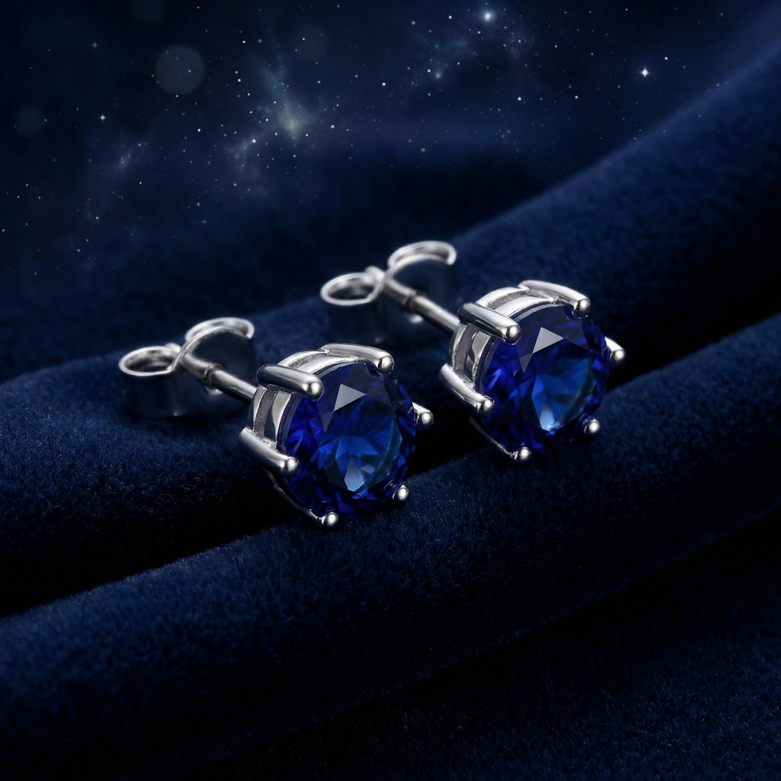 Round royal blue simulated sapphire stud earrings in sterling silver on dark blue velvet with a starry background.