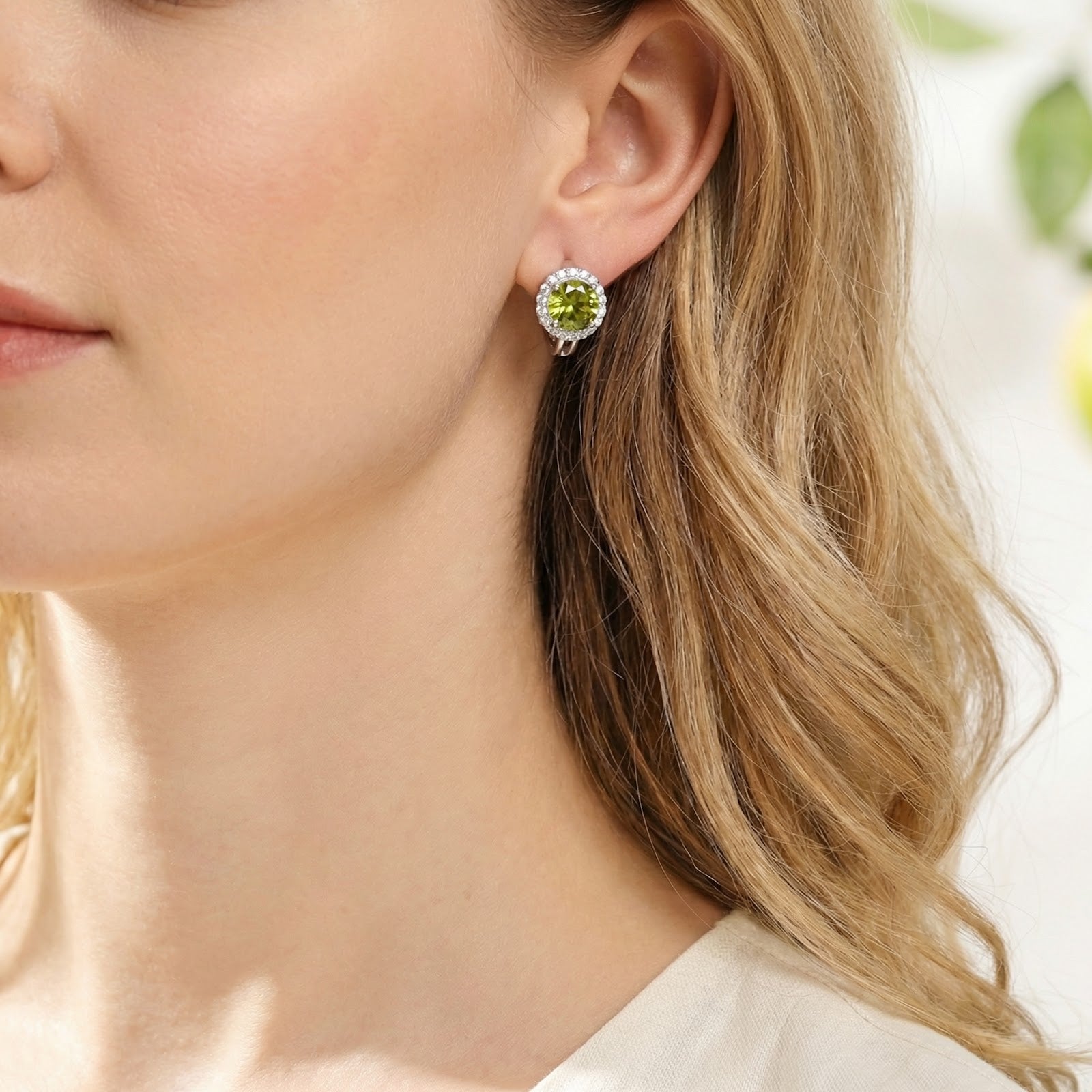 Close-up of a round green moissanite halo earring in sterling silver worn on a model's ear.