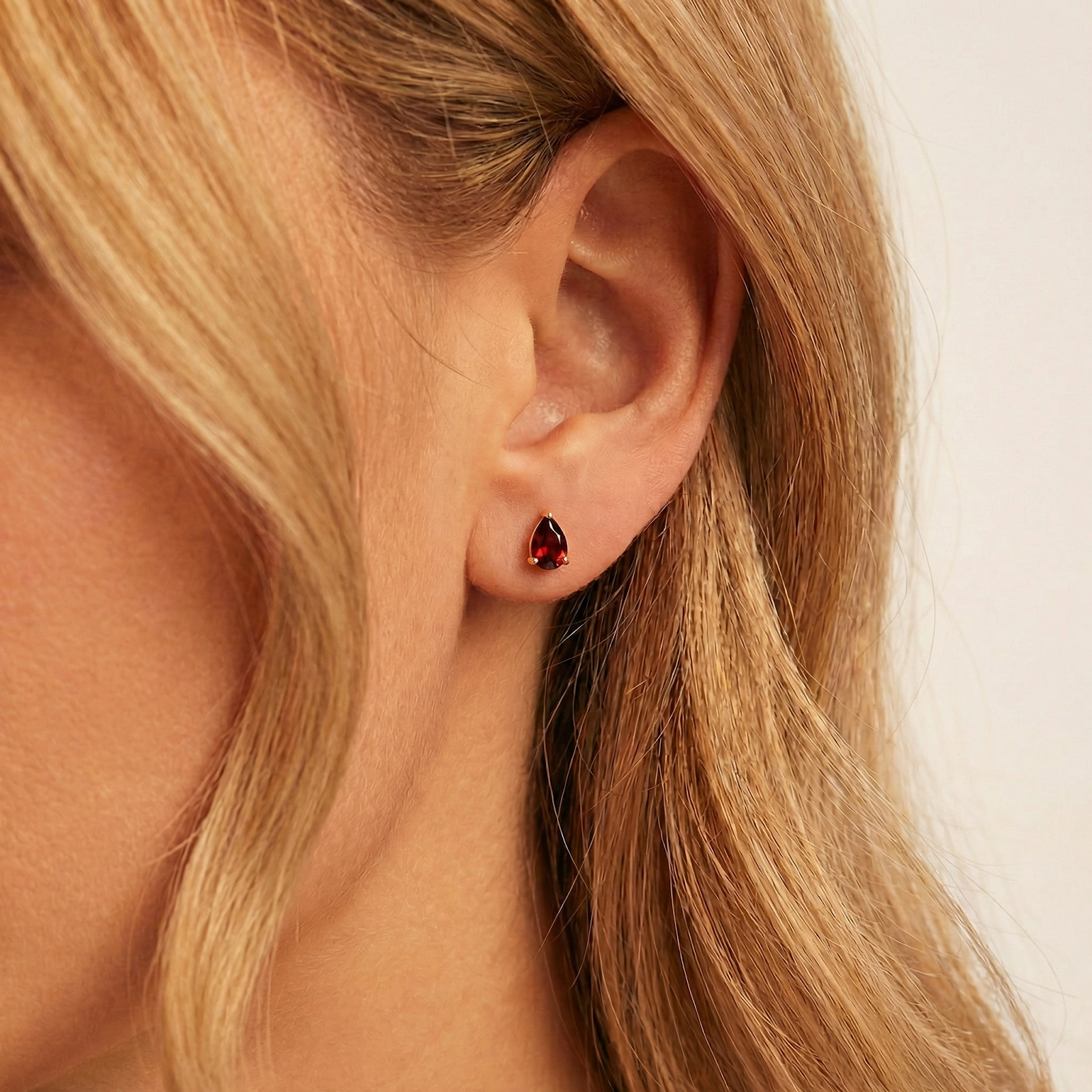 Side view of a pear cut simulated garnet stud earring in 18K gold vermeil worn on a woman's ear.