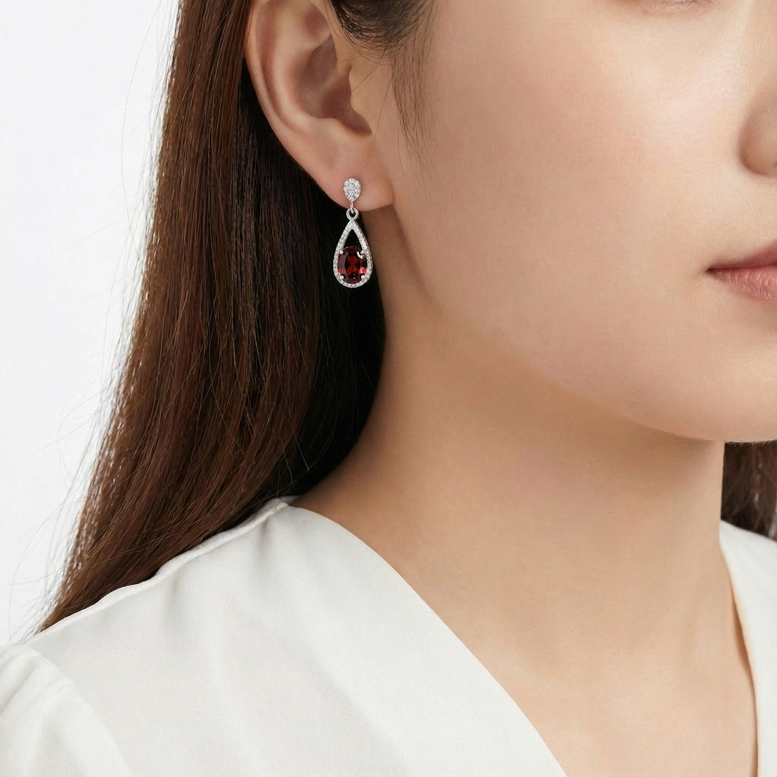 Woman wearing a simulated garnet and sterling silver teardrop drop earring against a plain background.