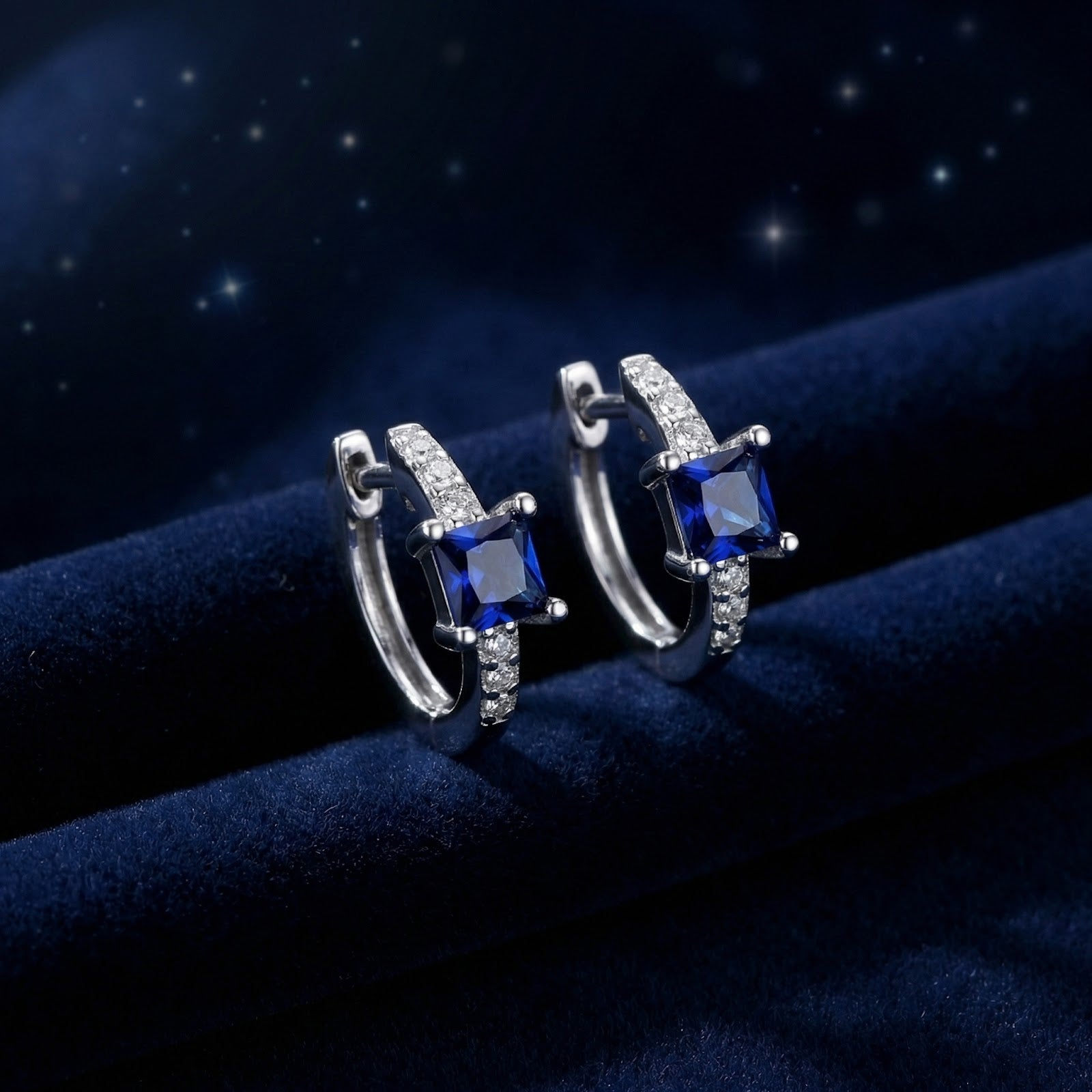 Square-cut simulated sapphire huggie earrings in S925 sterling silver on a dark blue velvet background.