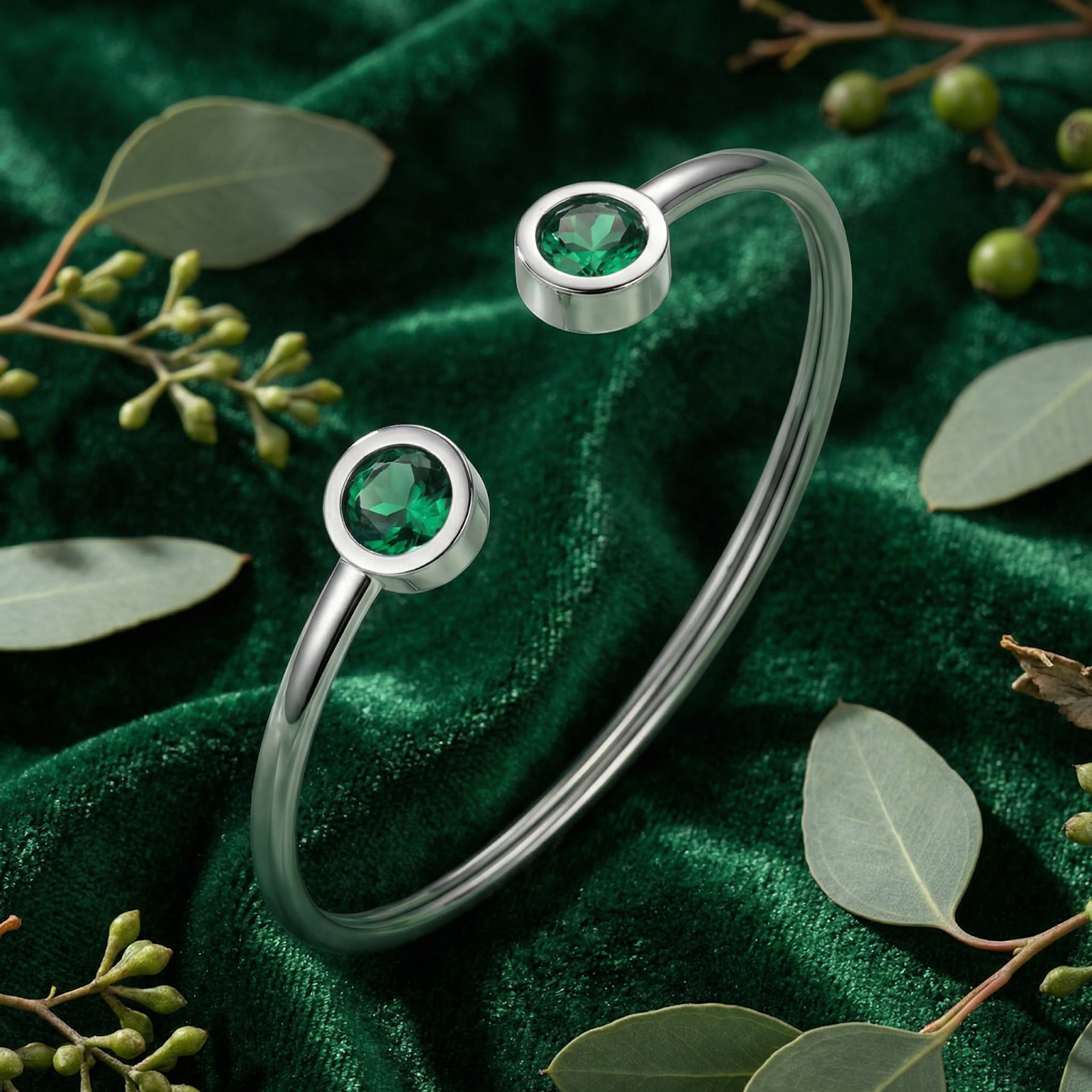 Silver stainless steel bypass cuff bracelet with round simulated emeralds on a green velvet lifestyle background.