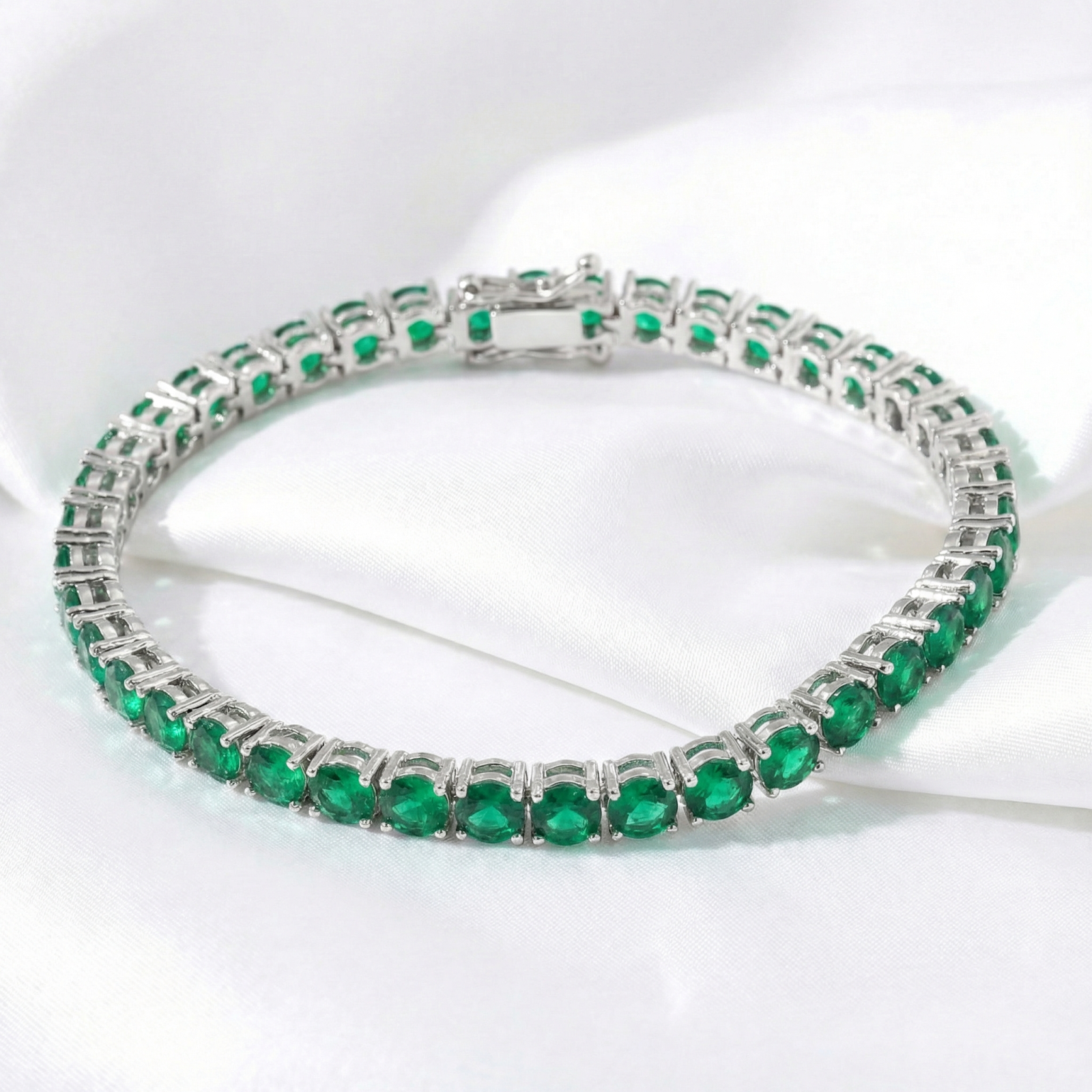 Vesperine tennis bracelet with round simulated emeralds in stainless steel on white silk.