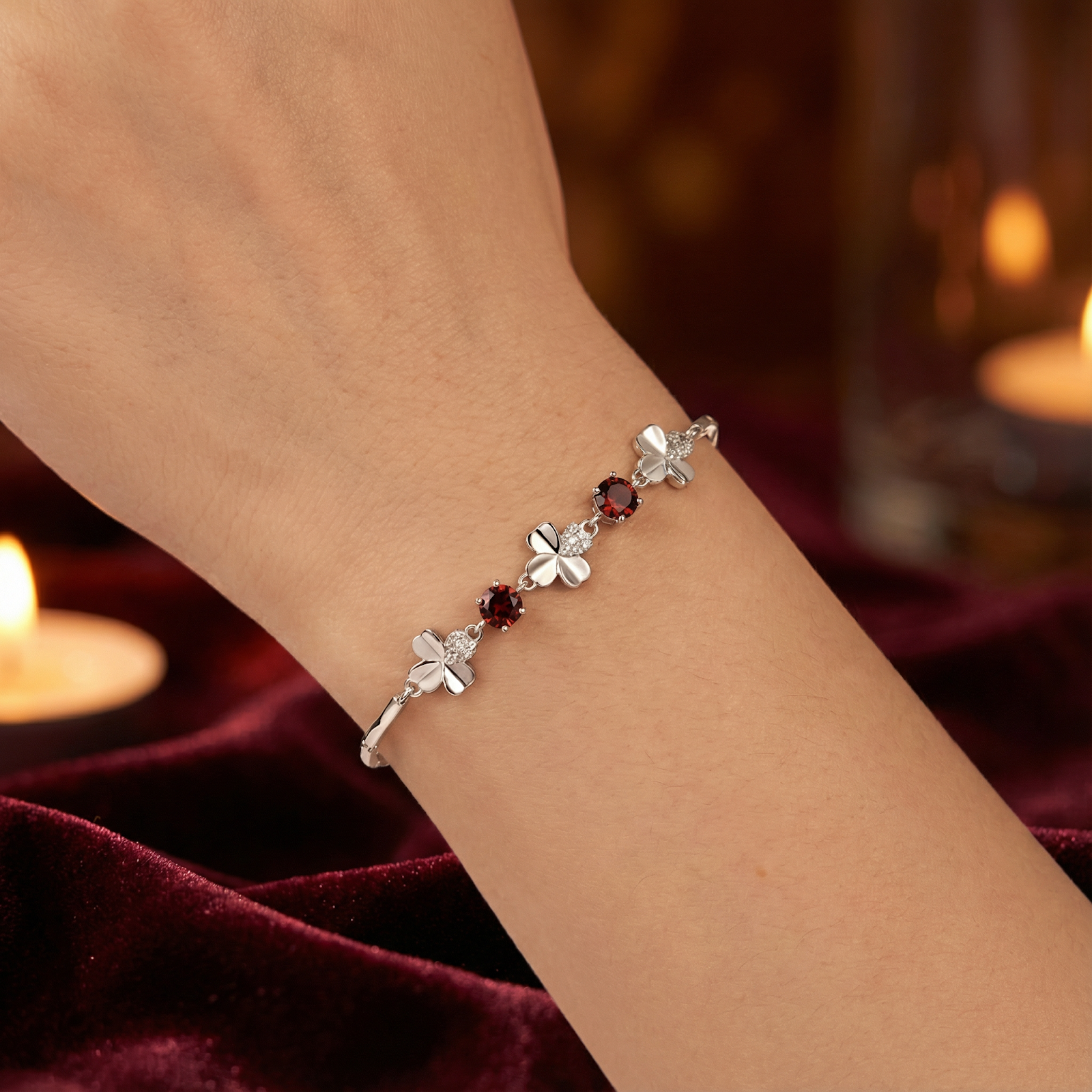 Close-up of the sterling silver clover bracelet with round-cut red garnets worn on a woman's wrist.