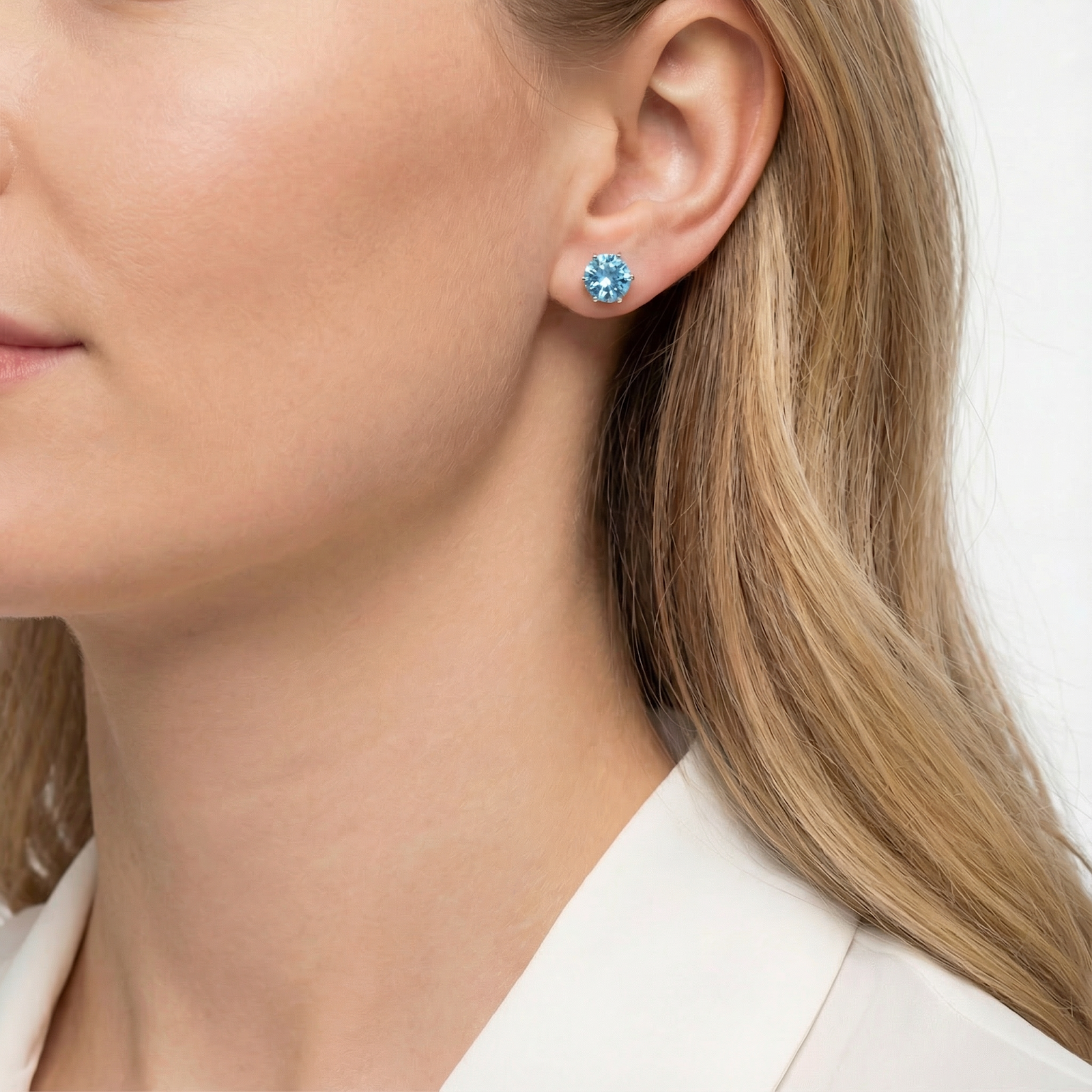 Close-up of a March birthstone simulated aquamarine stud earring worn on a woman's earlobe.