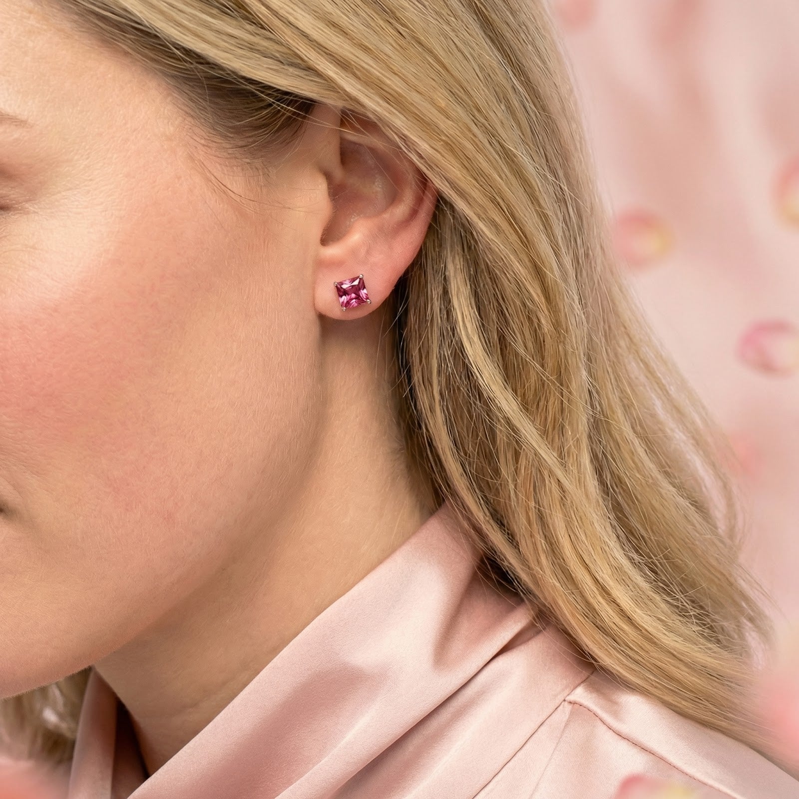 Blonde woman wearing a square cut pink tourmaline earring in rose gold vermeil against a pink background.