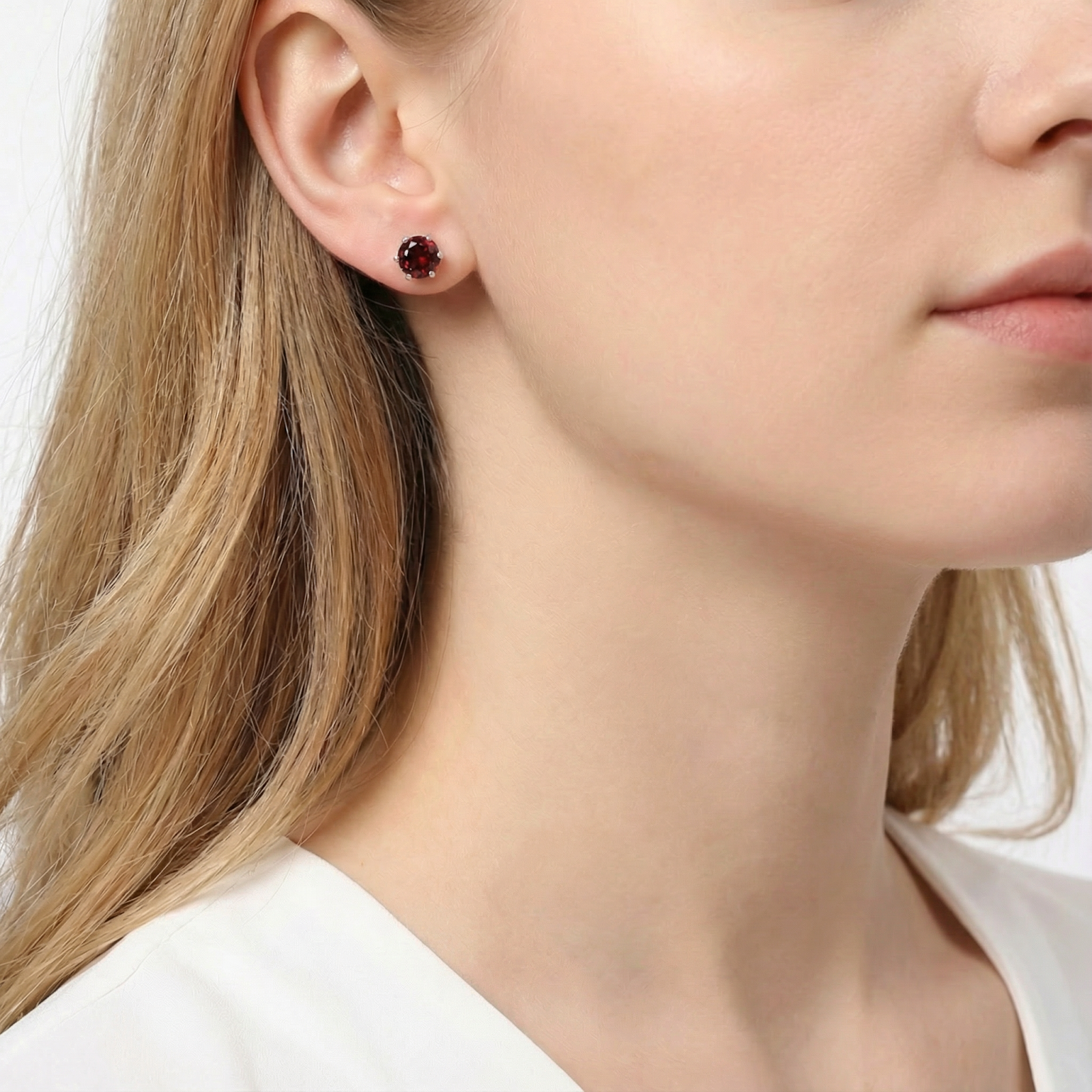 Woman wearing a round red garnet stud earring in sterling silver on her earlobe.
