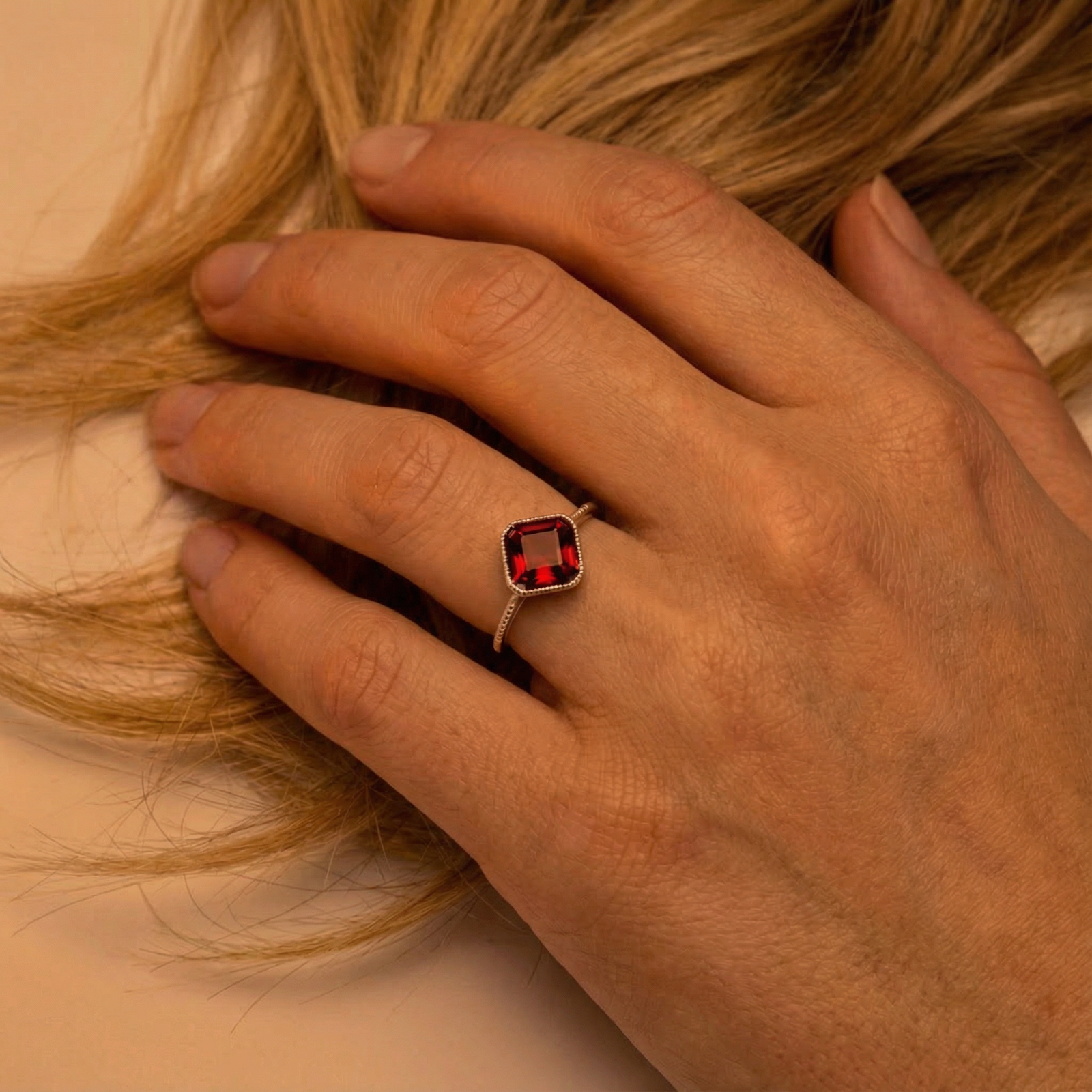 Sterling silver cushion-cut simulated garnet ring worn on a woman's hand resting on blonde hair.