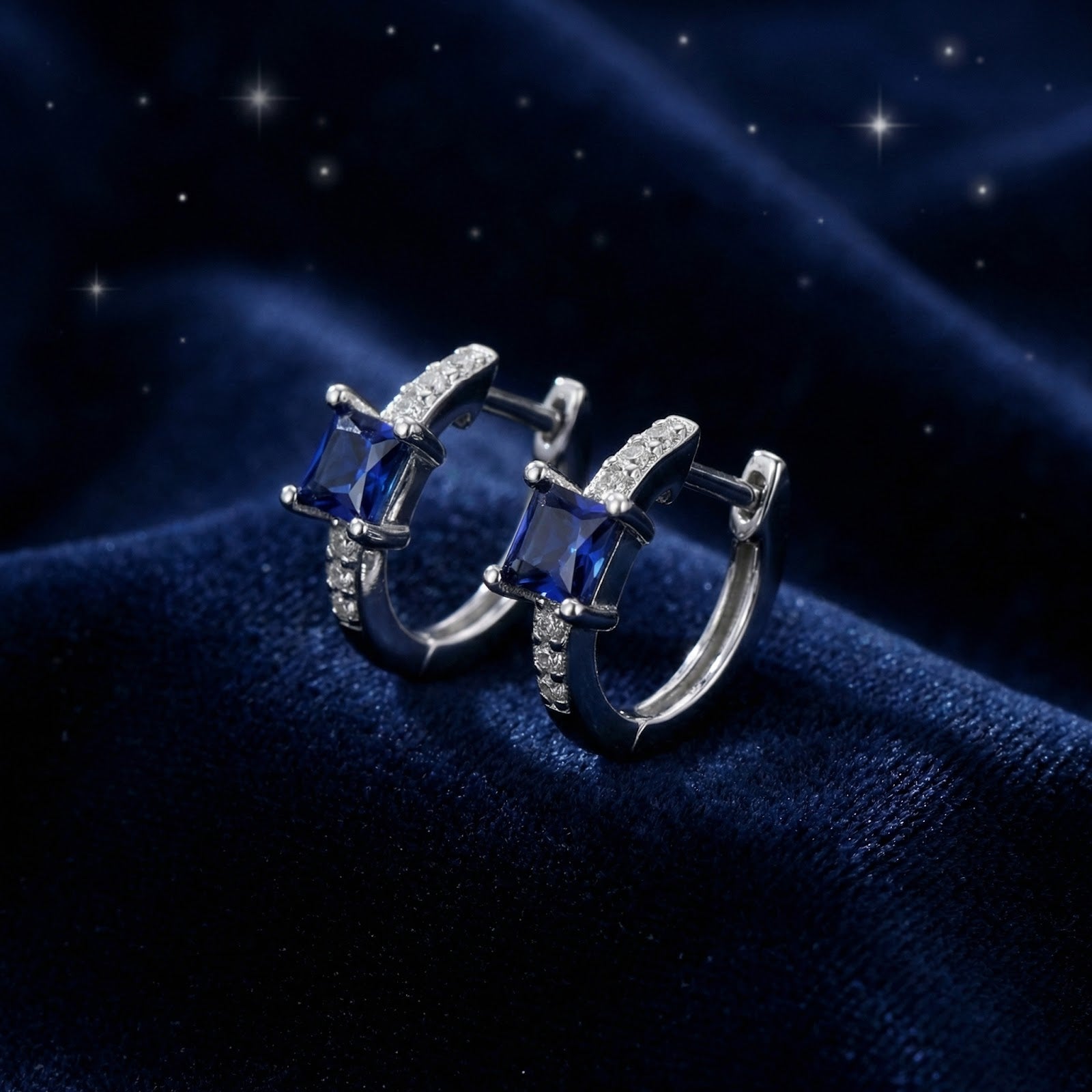 Side view of square-cut blue sapphire huggie earrings in sterling silver on a textured navy background.