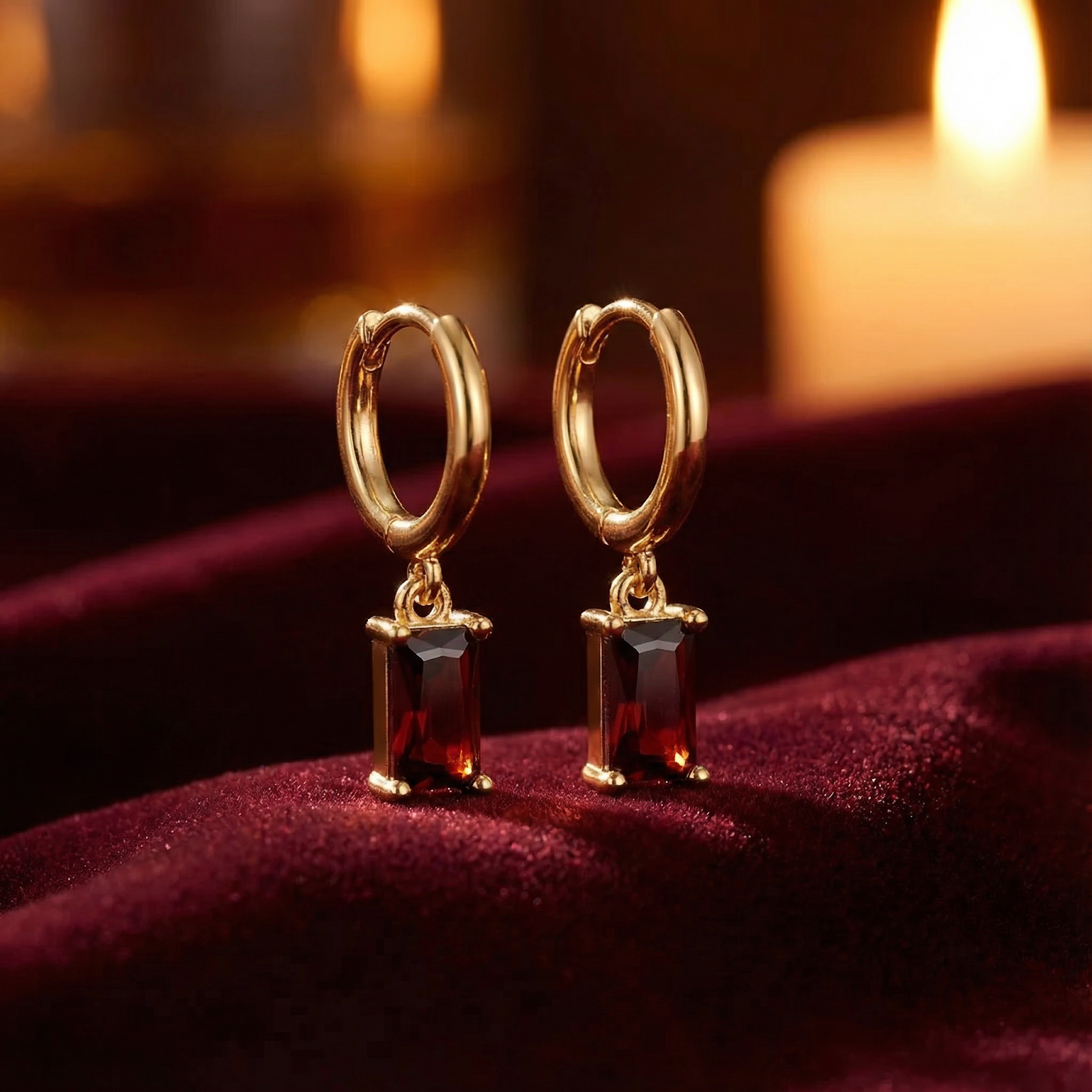 18K gold vermeil huggie earrings with emerald-cut simulated garnet stones on red velvet.