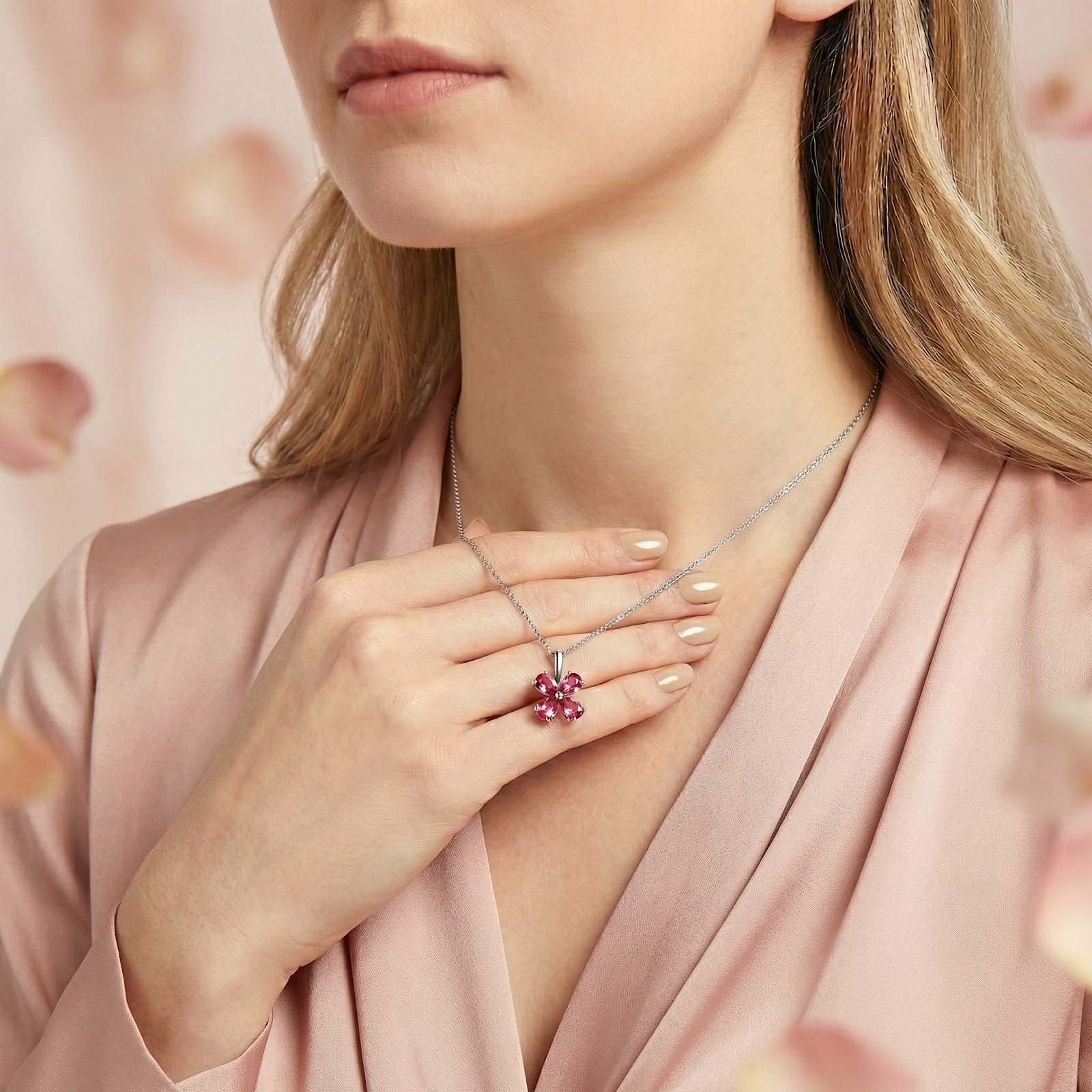 Petalina flower necklace in sterling silver with pink tourmaline stones worn by a model touching the pendant.