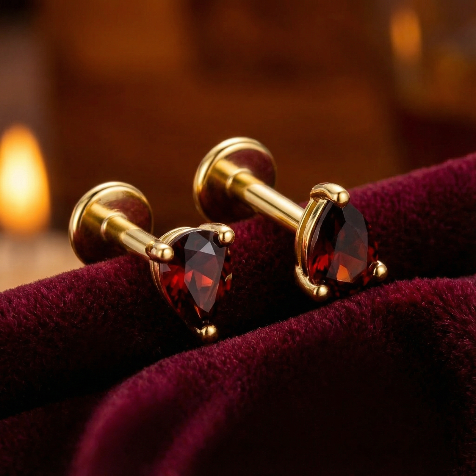 Close-up of pear cut simulated garnet stud earrings in 18K gold vermeil showing stone facets on red velvet.