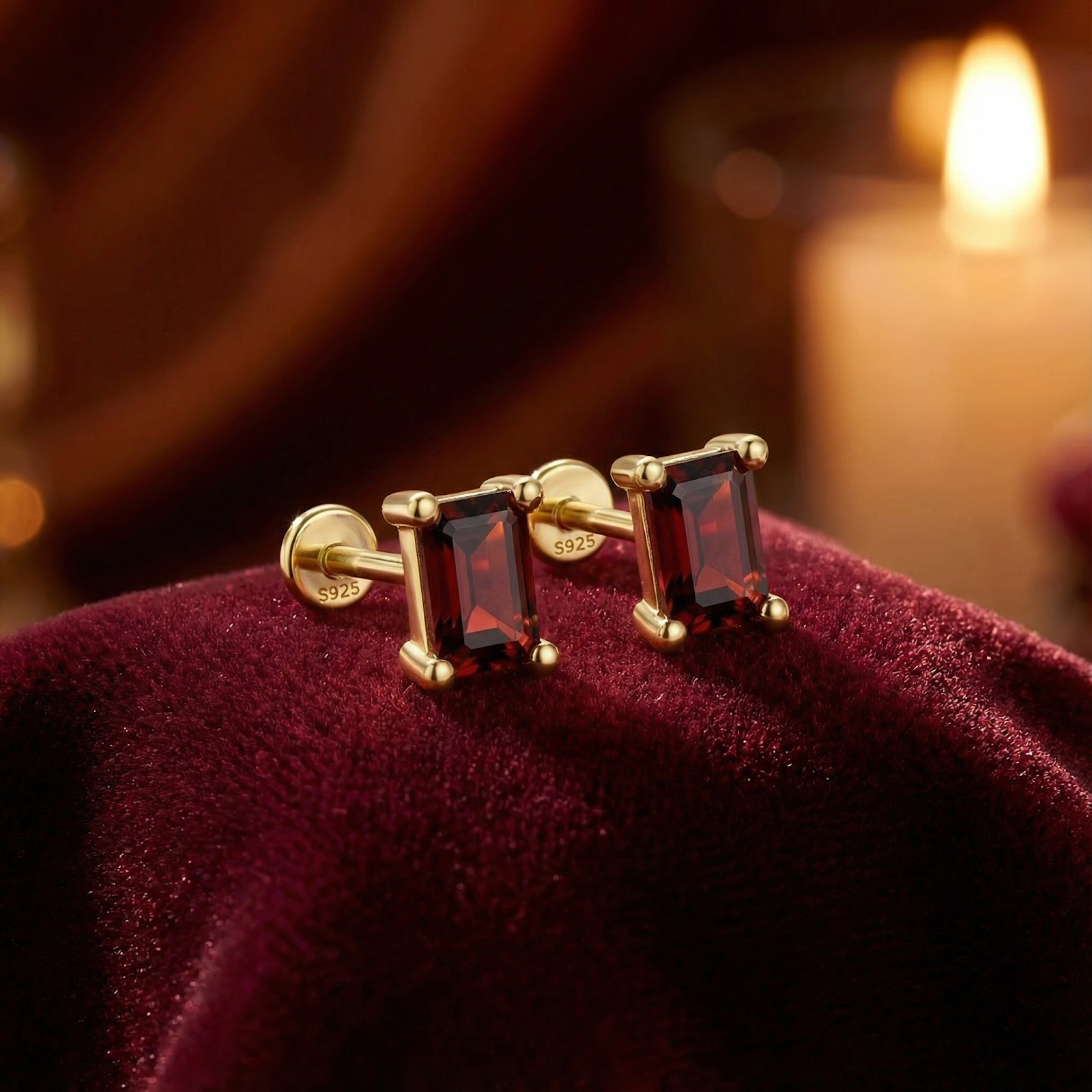Baguette cut simulated garnet stud earrings in 18K gold vermeil on red velvet with a candle background.