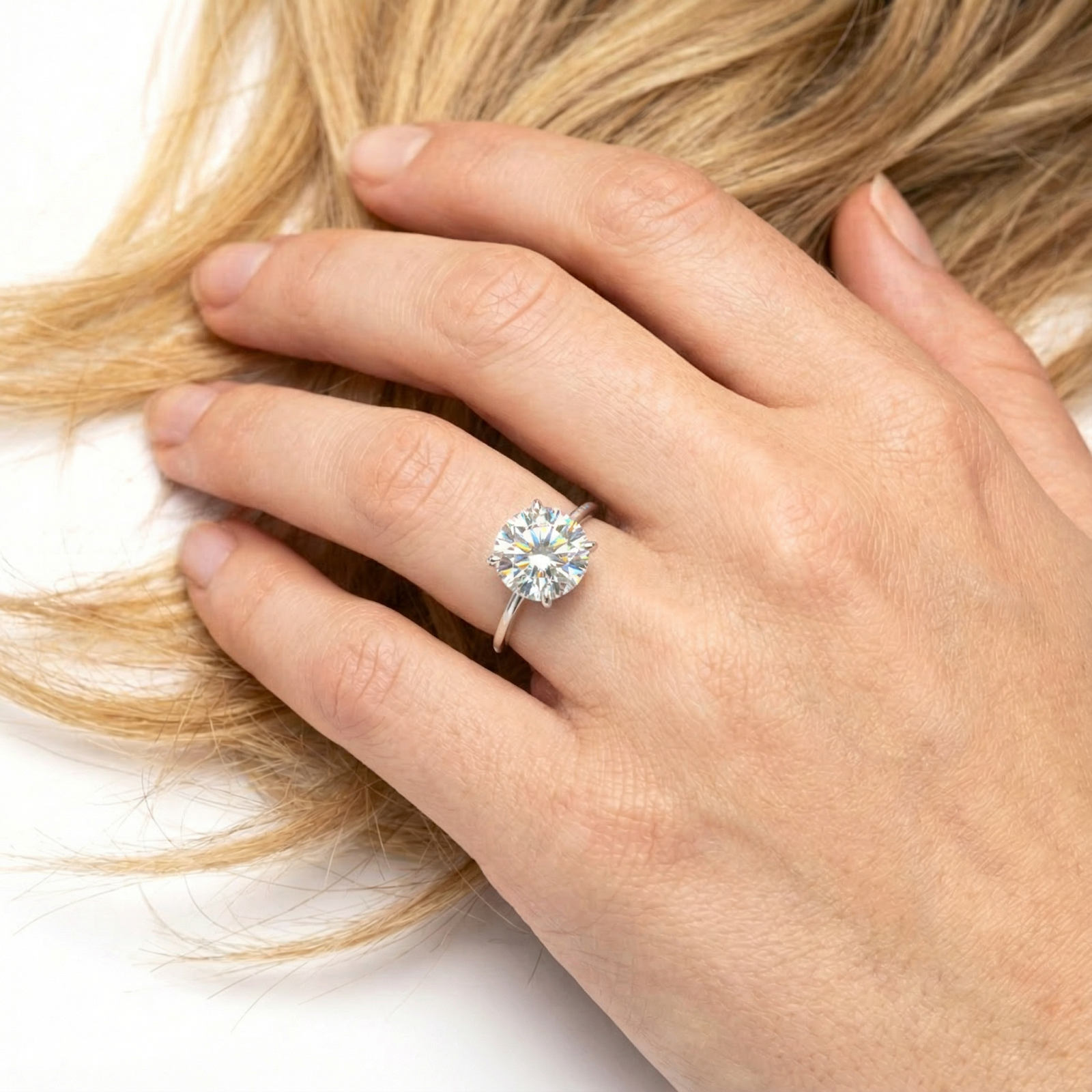 Round cut simulated diamond ring in sterling silver worn on a hand touching blonde hair.