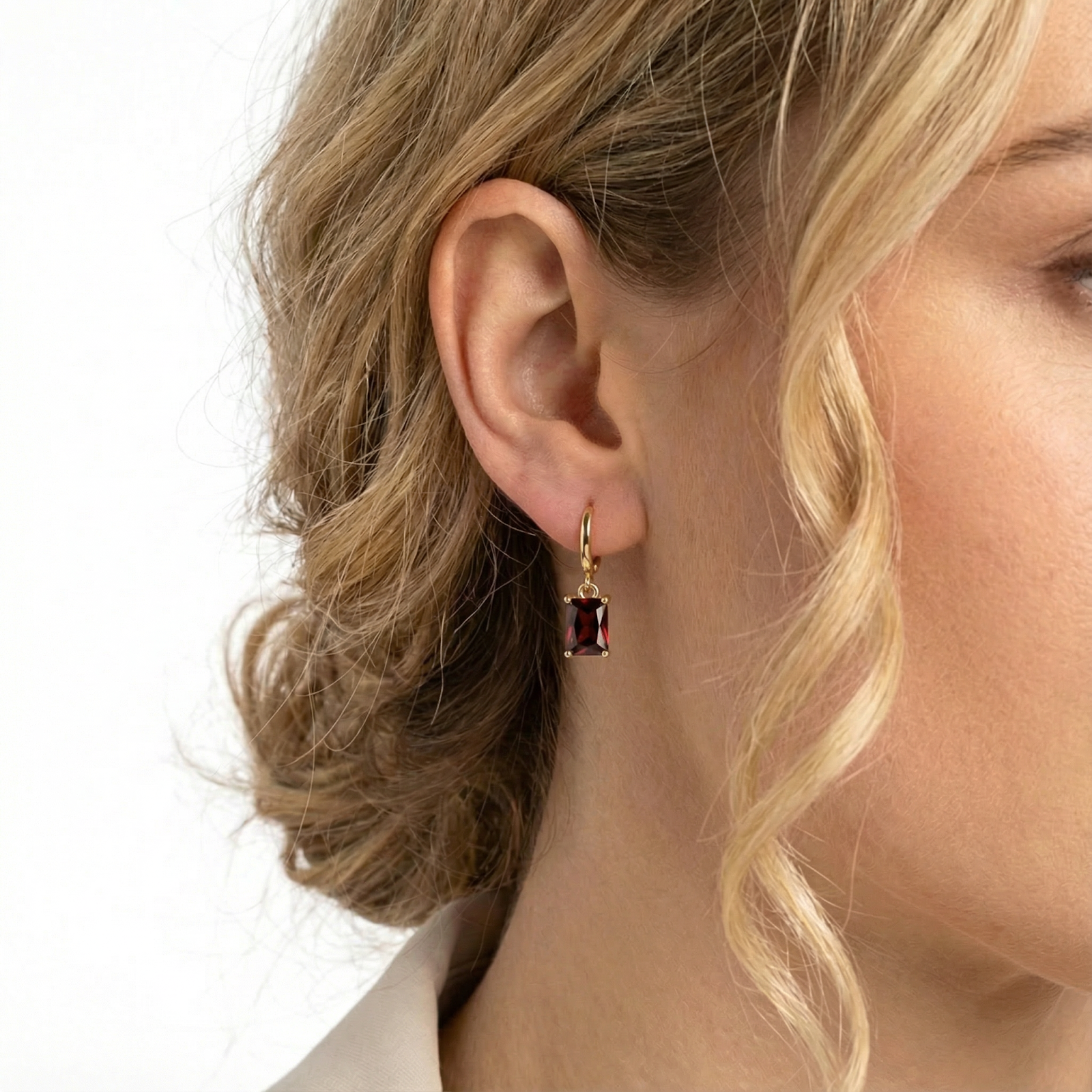 Side view of a model wearing an 18K gold vermeil huggie earring with an emerald-cut simulated garnet.