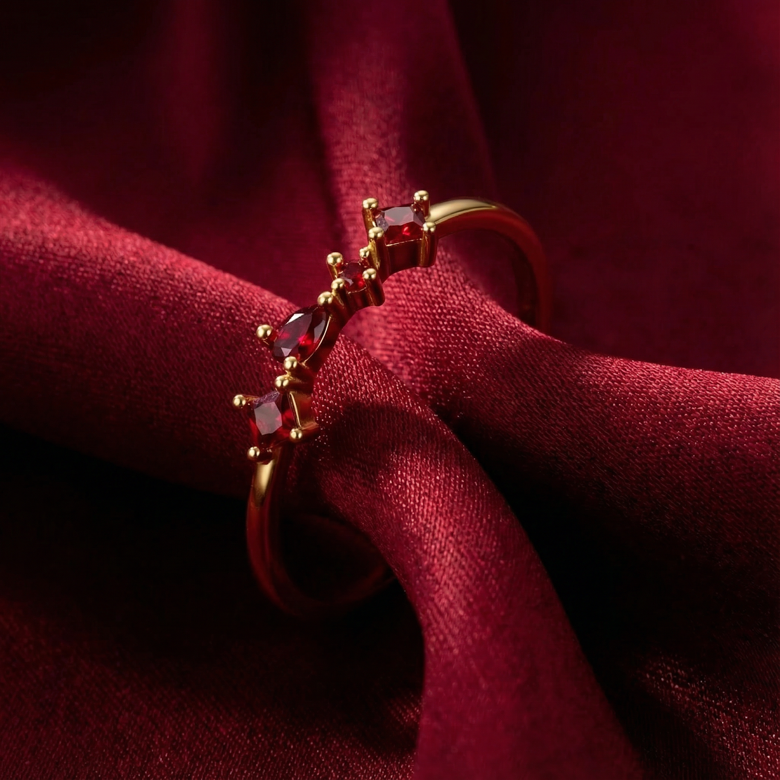 Julianna cluster ring in 18K gold vermeil with princess and pear cut simulated rubies on red fabric.