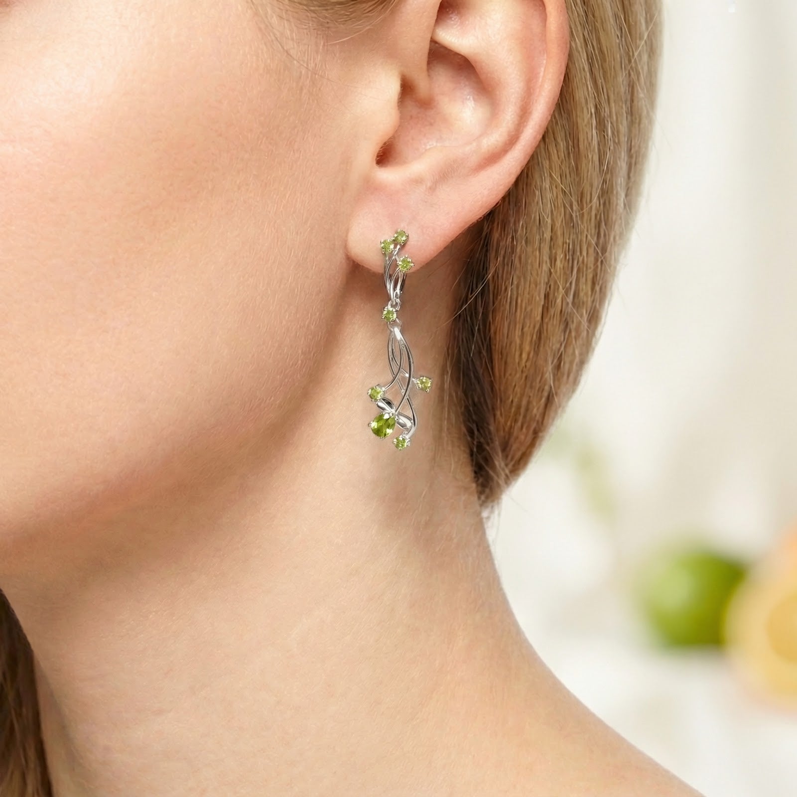 Side view of a sterling silver vine drop earring with green simulated peridot stones worn on an ear.