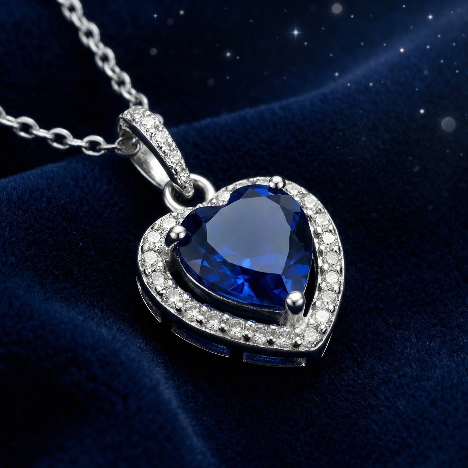 Close-up of a heart-cut simulated sapphire necklace in a sterling silver halo setting on blue velvet.