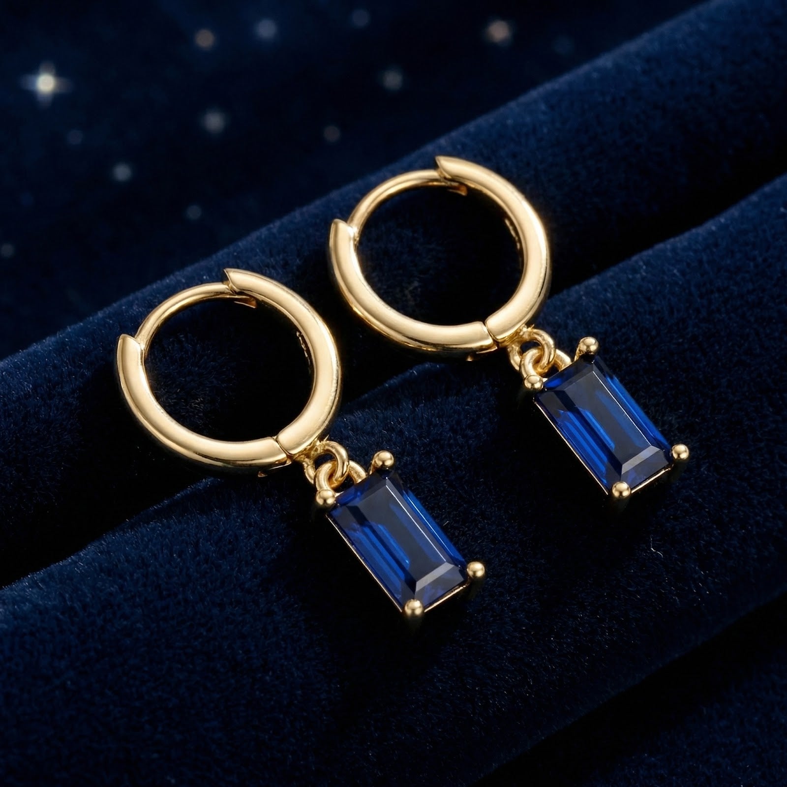Gold vermeil hoop earrings with emerald-cut simulated blue sapphire charms on blue velvet.