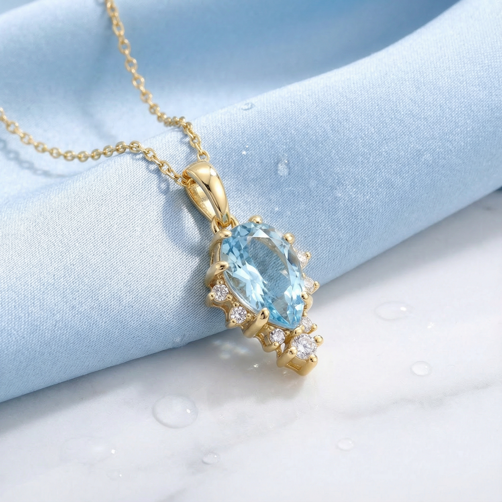 Angled view of the pear cut simulated aquamarine gold vermeil pendant on wet blue fabric.