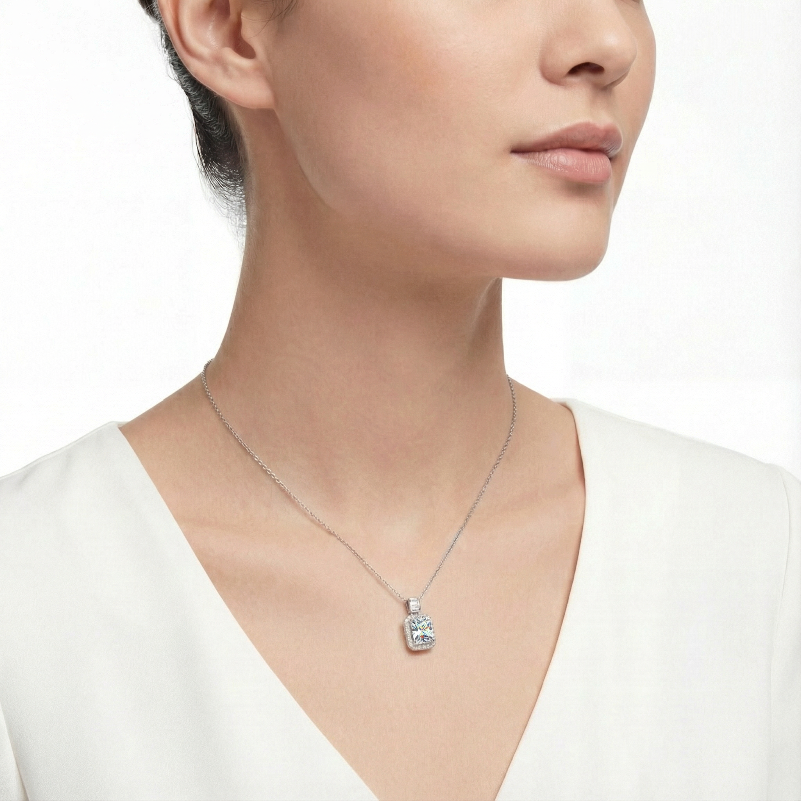 Model wearing the Aurella emerald cut zirconia halo necklace in silver, paired with a white V-neck top.