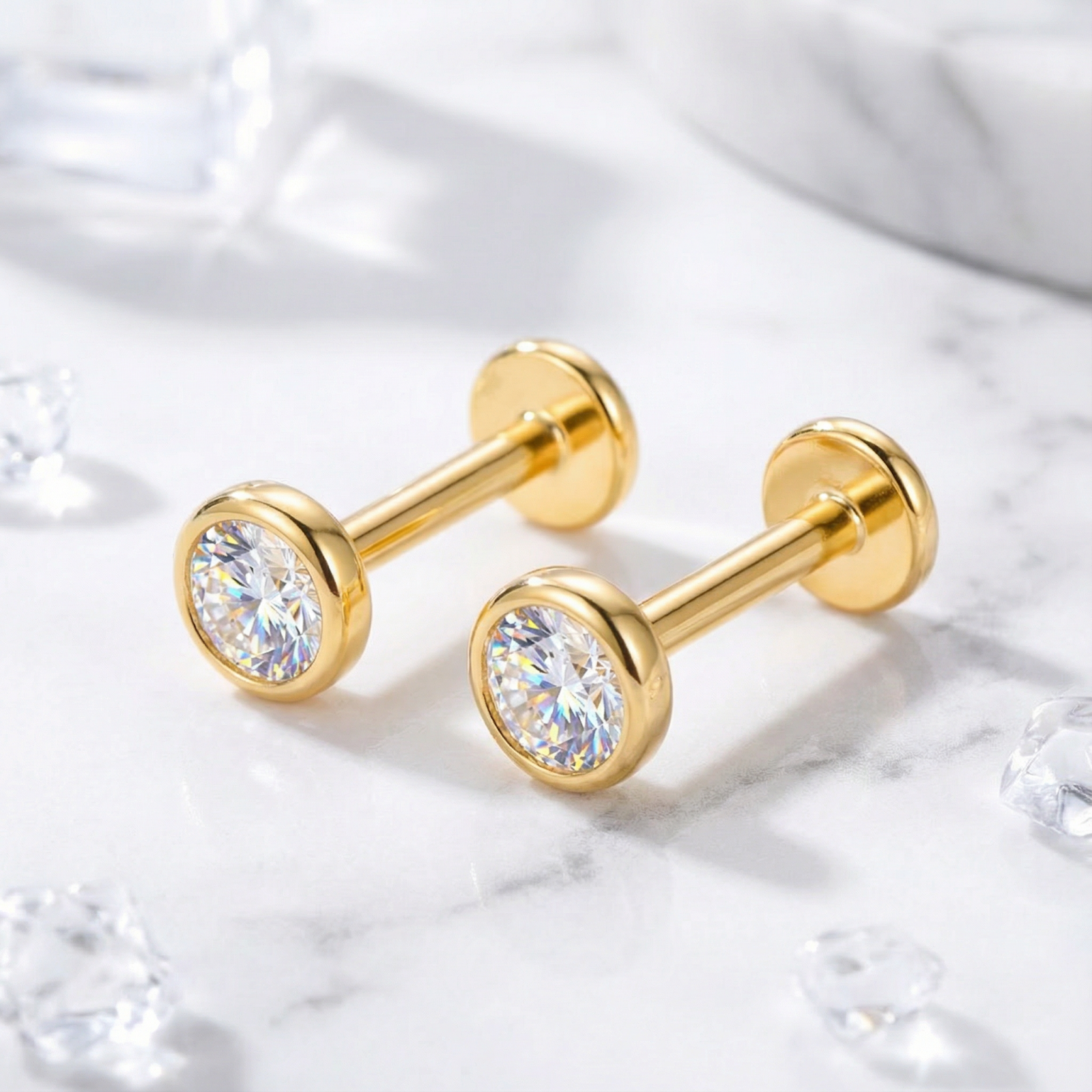 Gold vermeil bezel stud earrings with round zirconia stones and flat back posts on a marble surface.