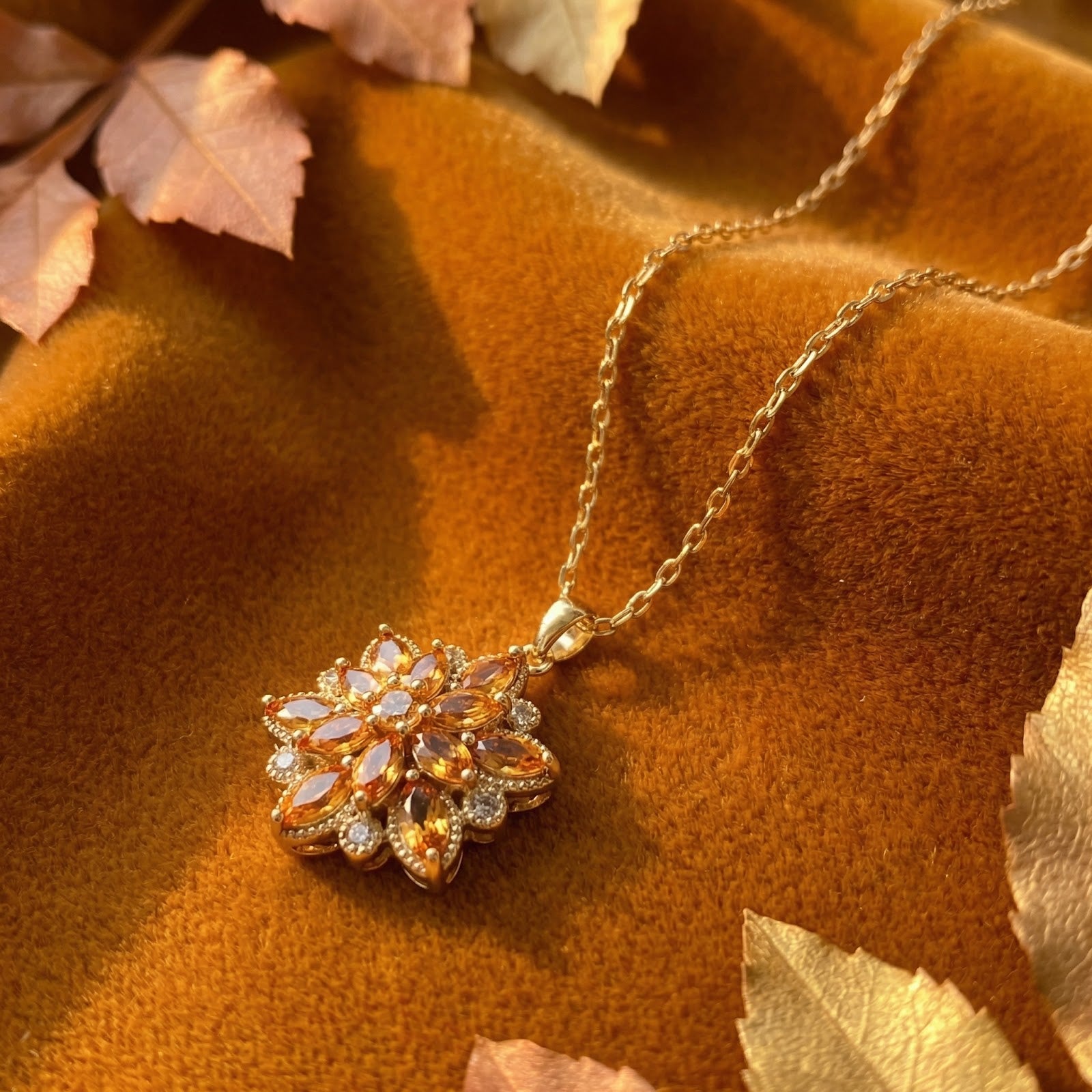 Gold finish stainless steel bloom necklace with yellow marquise stones on velvet with autumn leaves.