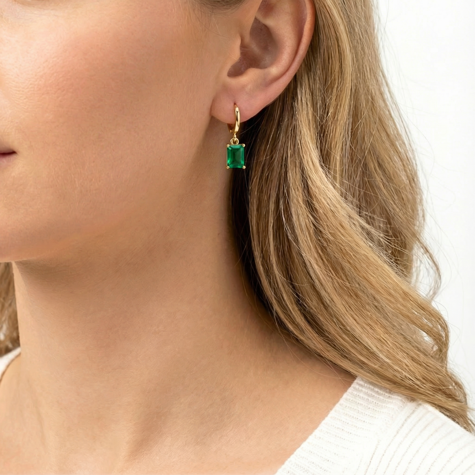 Side profile of a model wearing gold vermeil drop earrings with a deep green emerald-cut simulated stone.