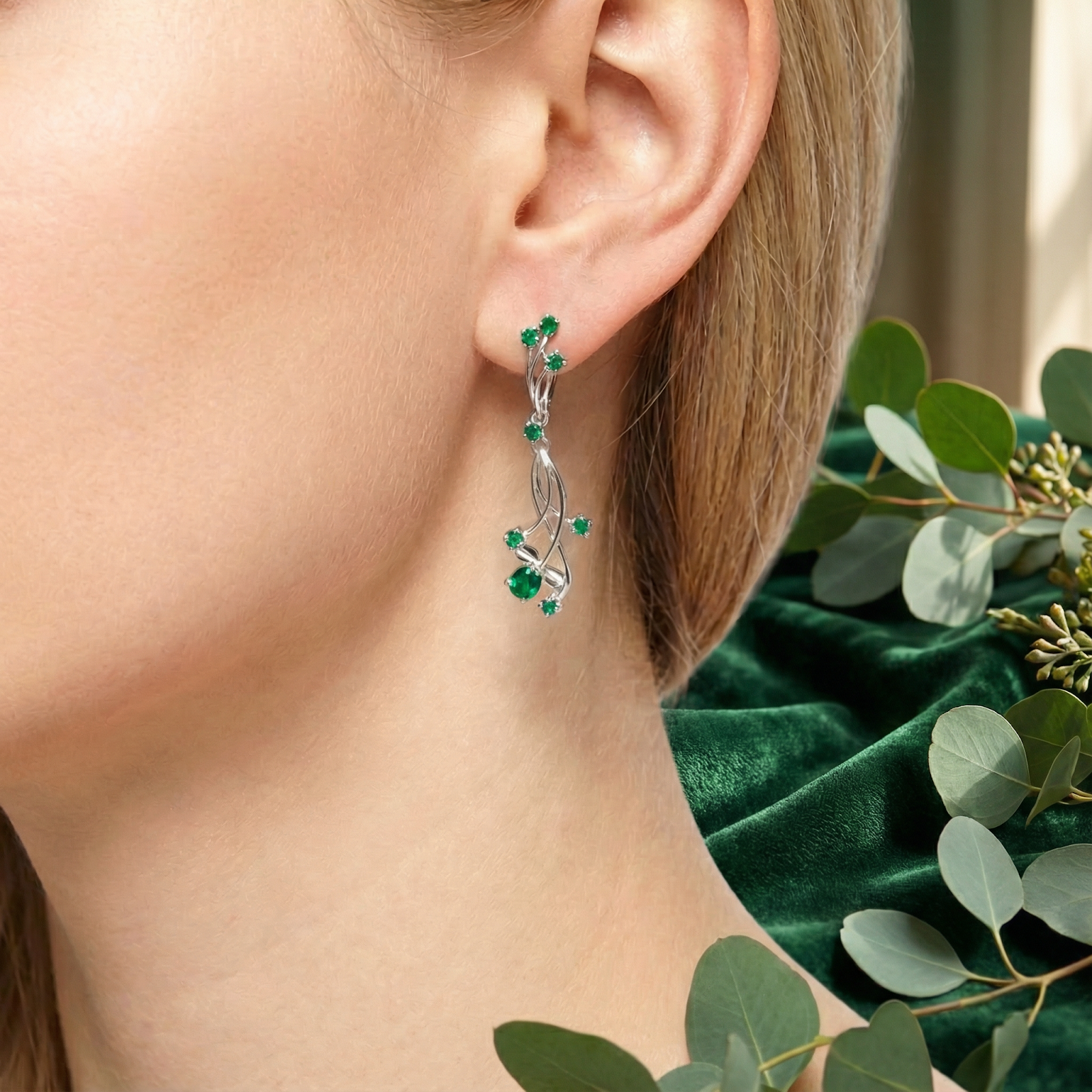 Close-up of a Calysia Vine sterling silver drop earring with pear and round cut simulated emeralds worn on an ear.