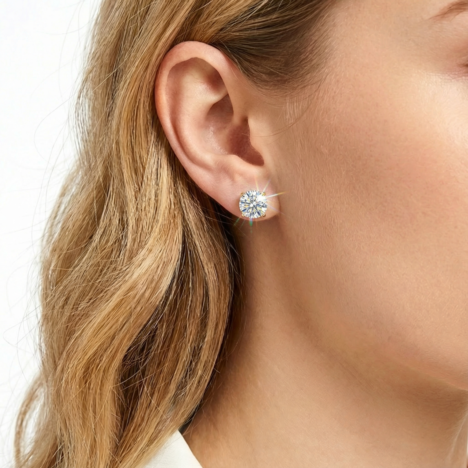 Woman wearing a gold stud earring with a sparkling round simulated diamond on her earlobe.