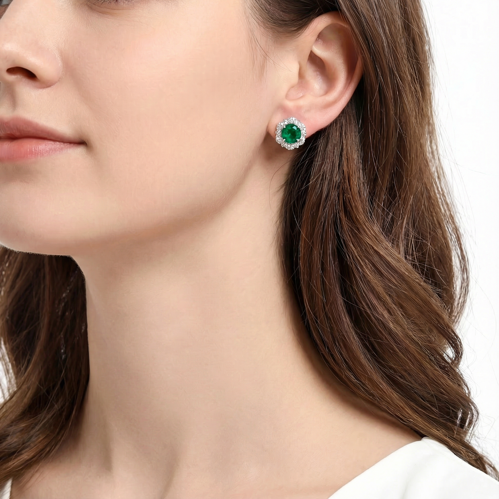 A woman wearing the Valeriana sterling silver halo stud earrings with round vivid green simulated emeralds.