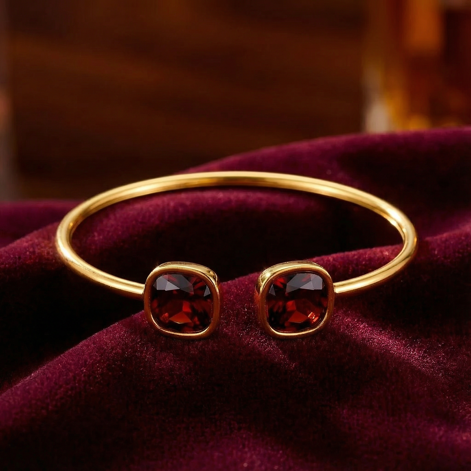Close-up of gold stainless steel cuff bracelet with two square cushion-cut red simulated garnets.
