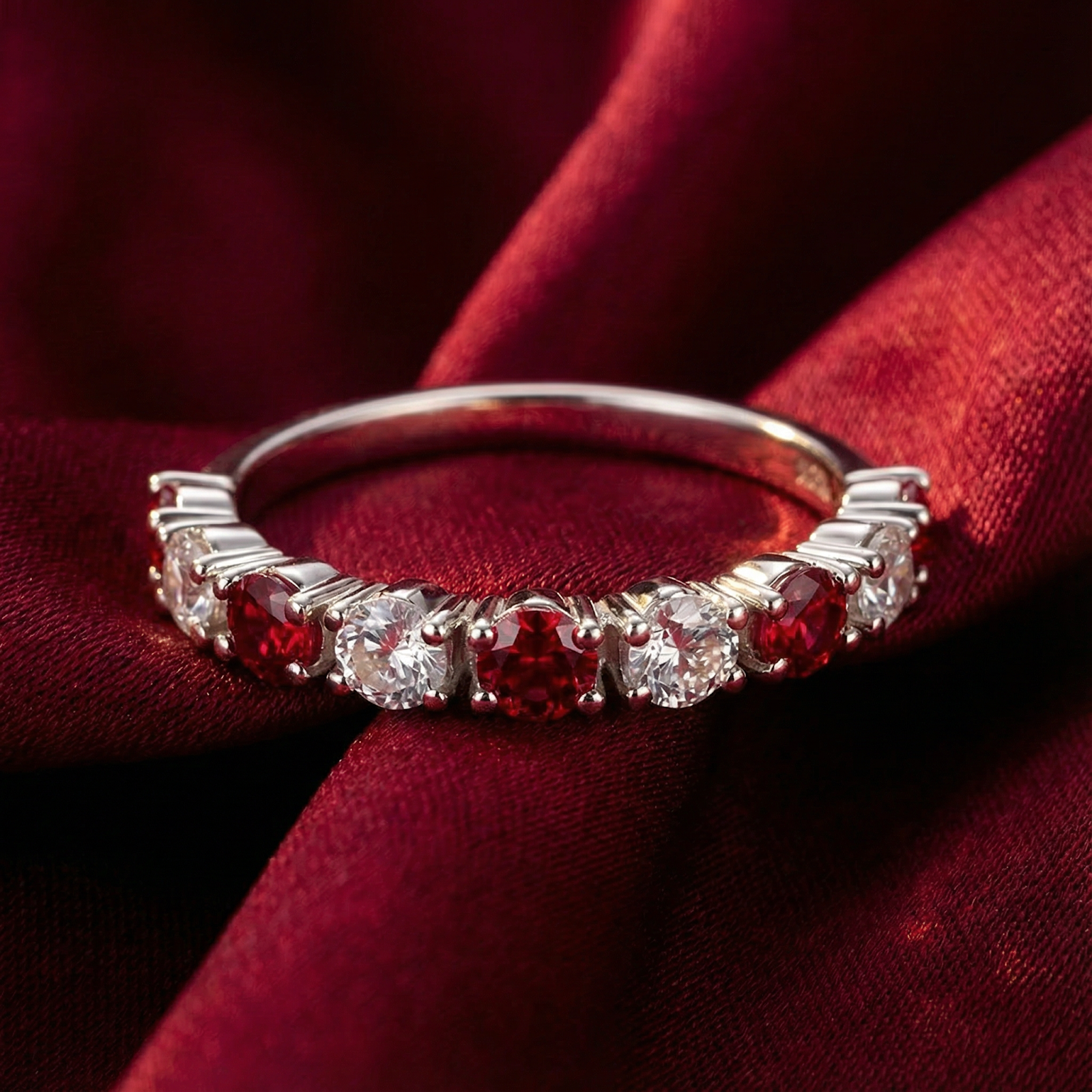 Rubielle S925 sterling silver half-eternity ring with round-cut red and clear stones resting on red silk fabric.