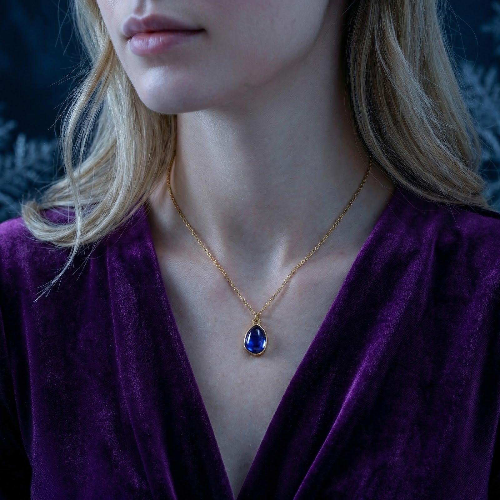 Model wearing the gold stainless steel Amelise teardrop necklace with a blue simulated tanzanite pendant.